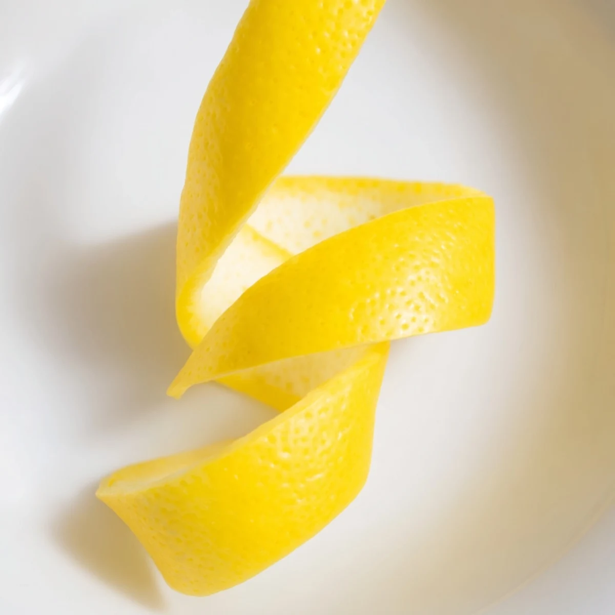 Close-up of a lemon twist garnish, with oils about to burst and add a zesty finish to a treat.