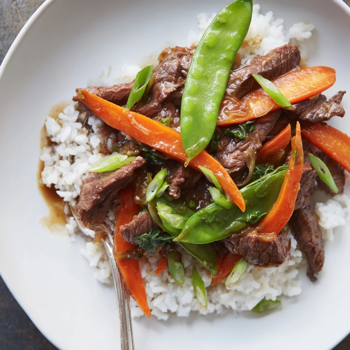 Close-up of sizzling Beef Stir Fry with Snow Peas and Carrots glistening with savory sauce.