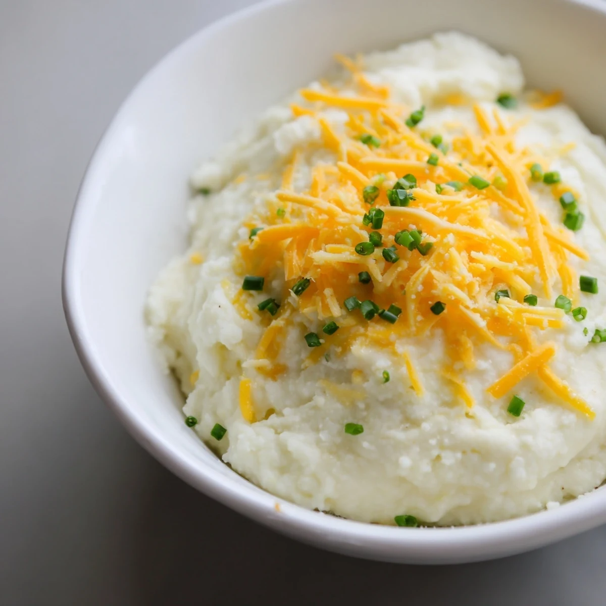 Creamy Garlic Mashed Cauliflower with Cheese topped with fresh chives in a white serving bowl.