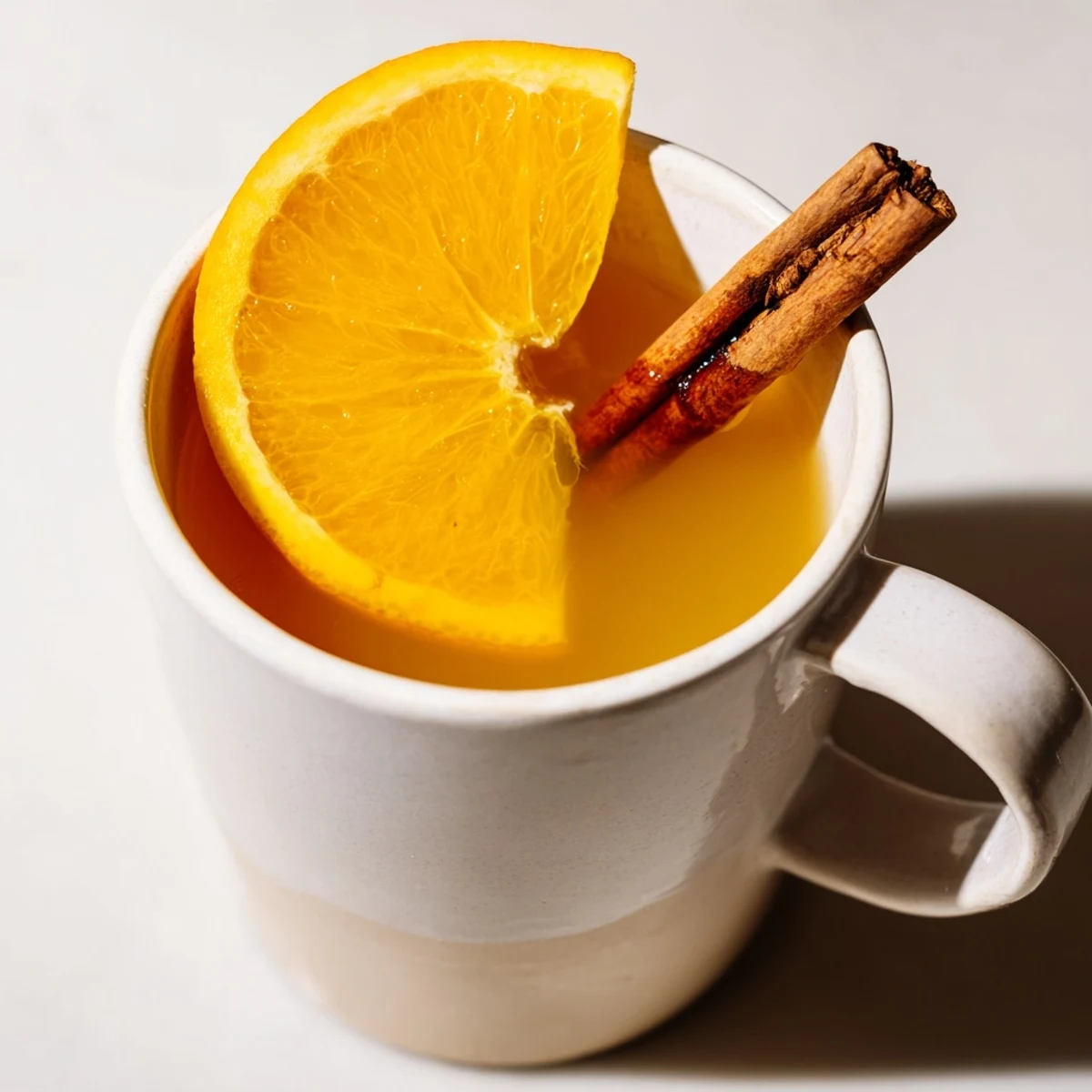 Steaming mugs of spiced hot apple juice with cinnamon, garnished with an orange slice.