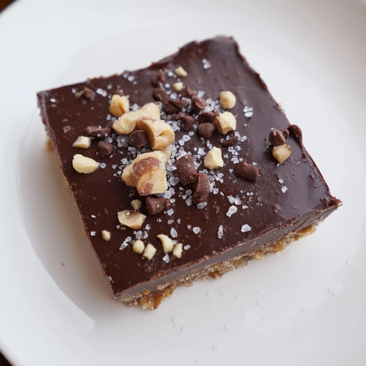 Chocolate Treat Bar squares stacked on a white plate with sea salt flakes and a cup of coffee nearby. 