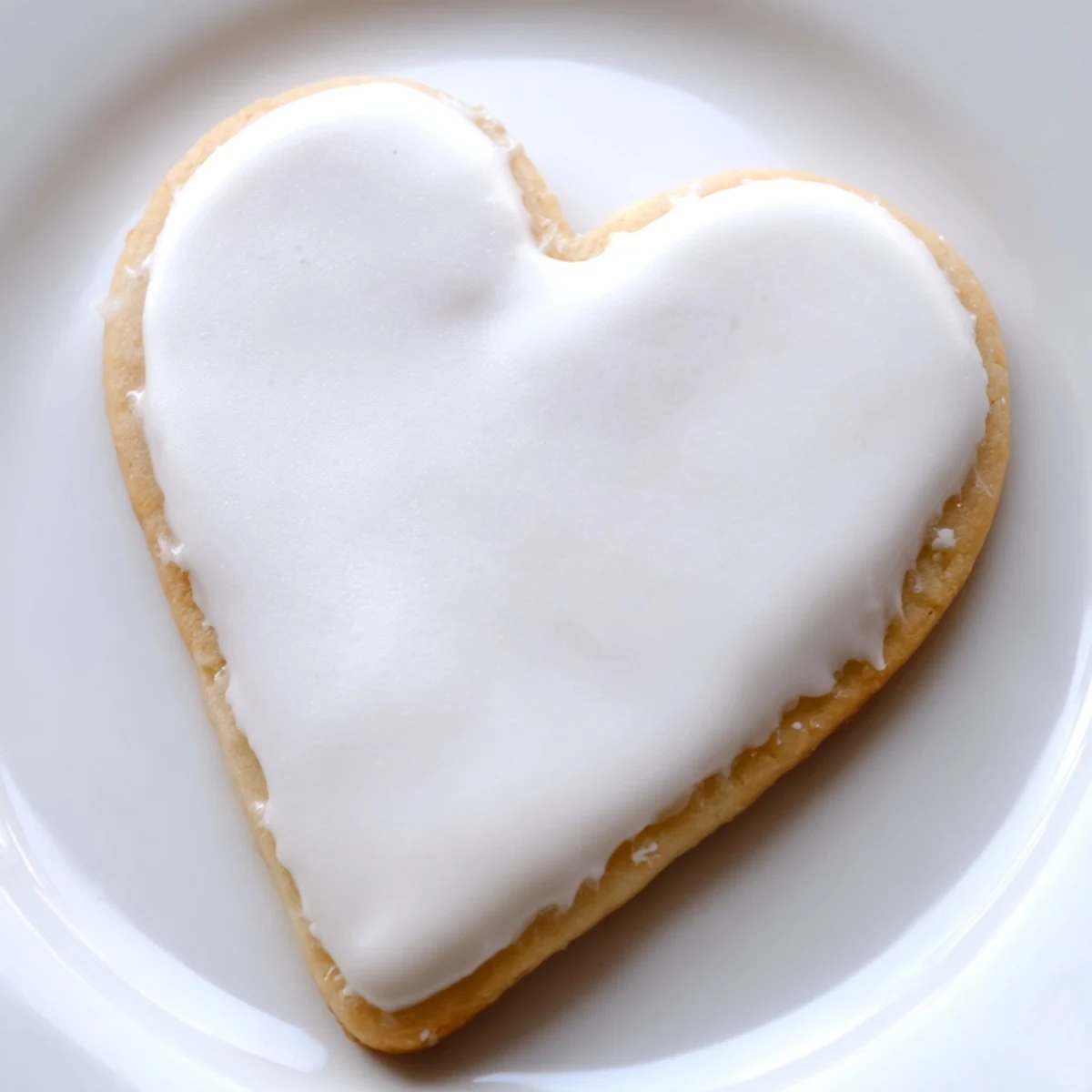 Two Heart Shaped Sugar Cookies with Royal Icing are decorated with pink swirls, arranged on a marble countertop with a vintage spoon.