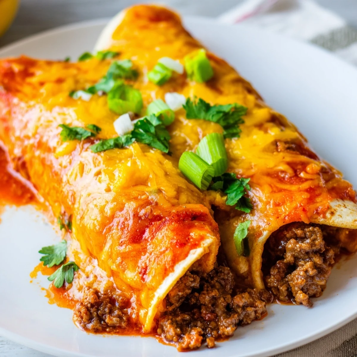 Steam rises from saucy Beef Enchiladas with Red Enchilada Sauce, served hot with a side of sour cream and sliced avocados.