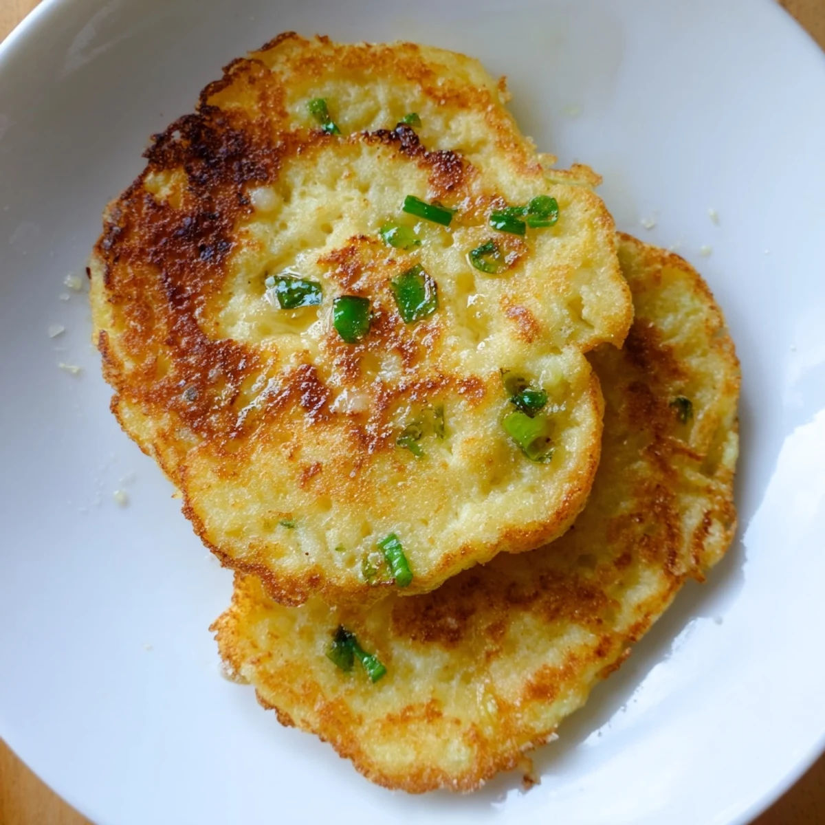 Freshly cooked Irish Boxty Potato Pancakes with Scallions stacked on a plate, garnished with extra green onions and served alongside sour cream.