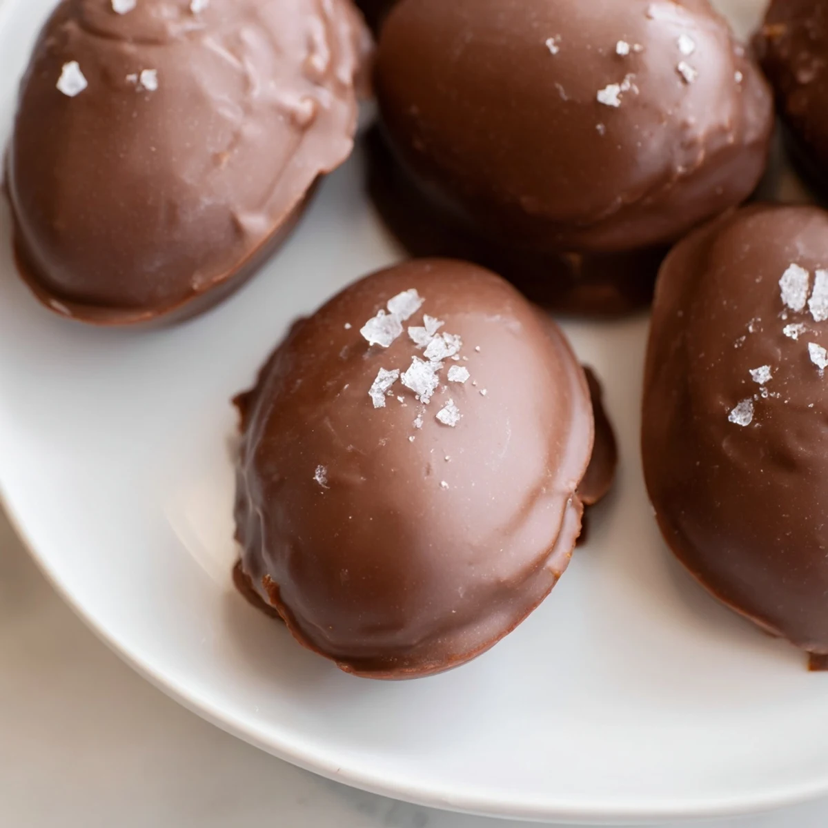 Freshly dipped chocolate peanut butter eggs resting on parchment paper, with glossy dark chocolate coating and a creamy peanut butter center.  