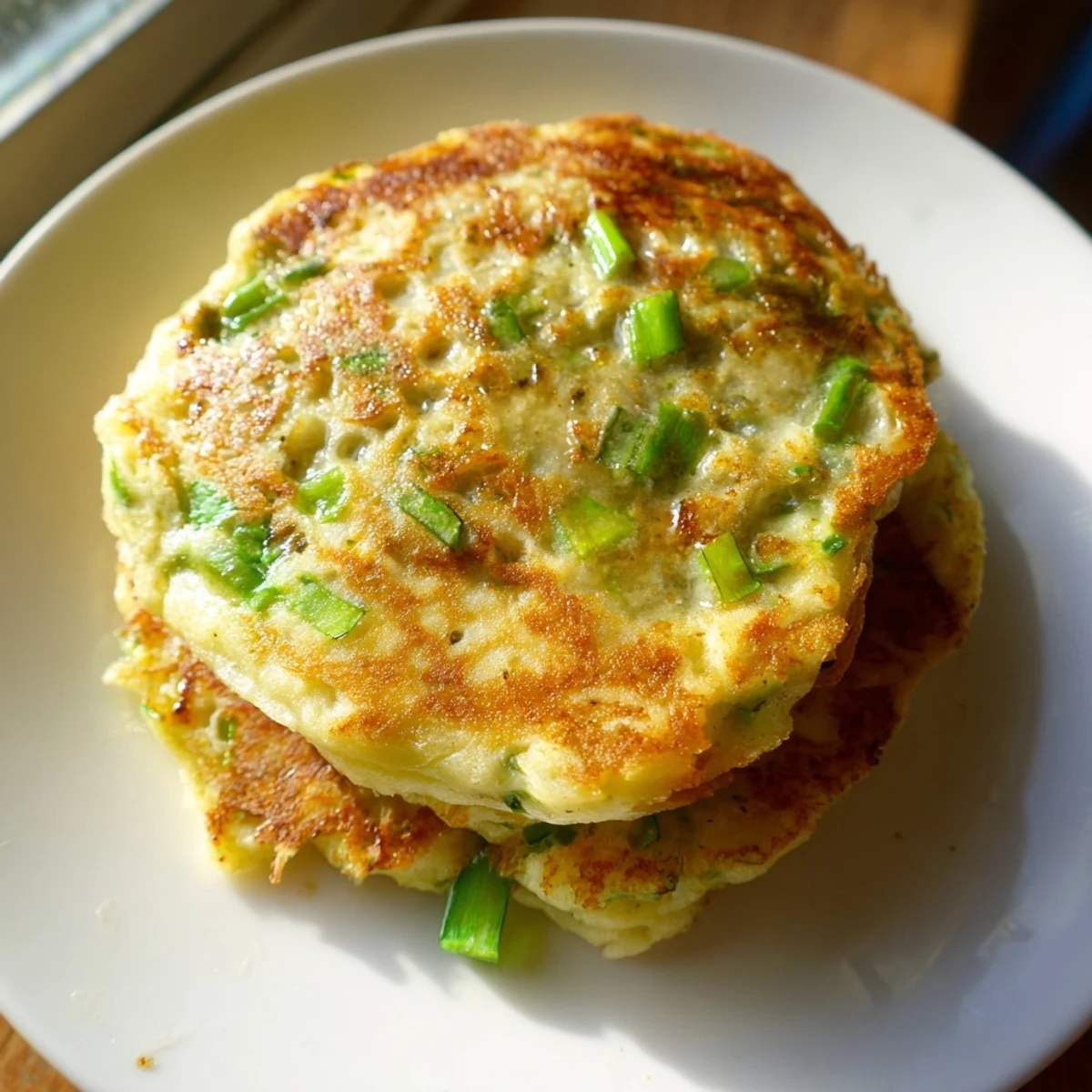 Golden-brown Irish Boxty Potato Pancakes with Scallions sizzle in a skillet, releasing a savory, buttery aroma.
