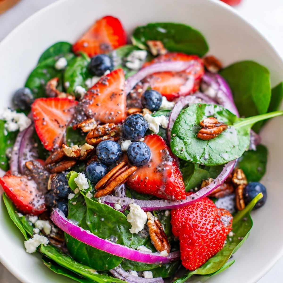 Fresh baby spinach and sliced strawberries in Strawberry Spinach Salad with Poppy Seed Dressing, topped with crunchy pecans and creamy feta cheese.
