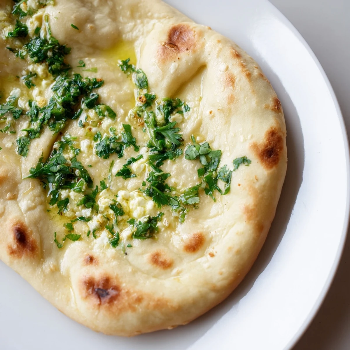 Freshly cooked Cottage Cheese Garlic Naan on a skillet with garlic butter, cilantro garnish, and steam rising from the bread.