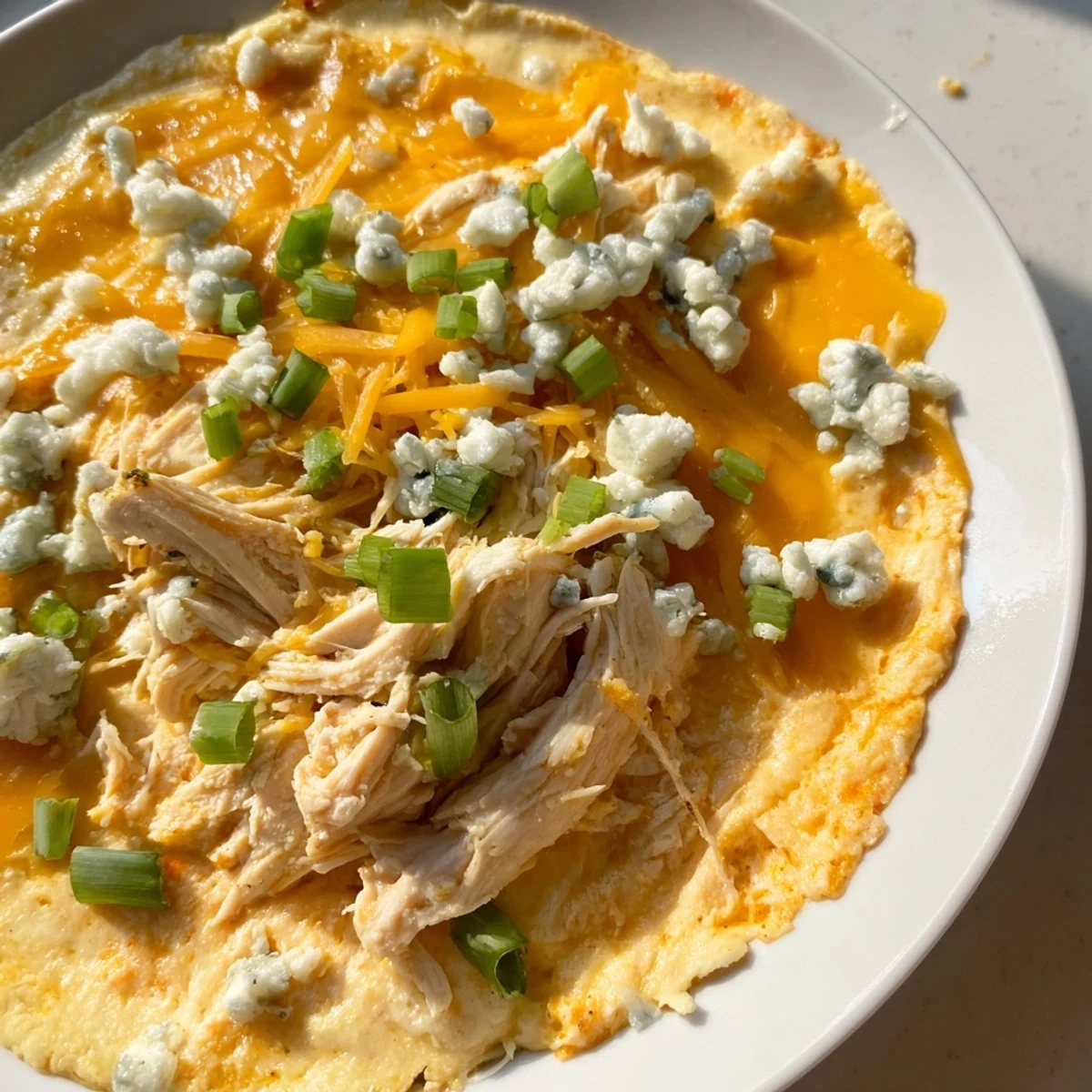 A close-up of bubbling Keto Buffalo Chicken Dip in a baking dish, topped with melted cheese and green onions, with celery sticks on the side.