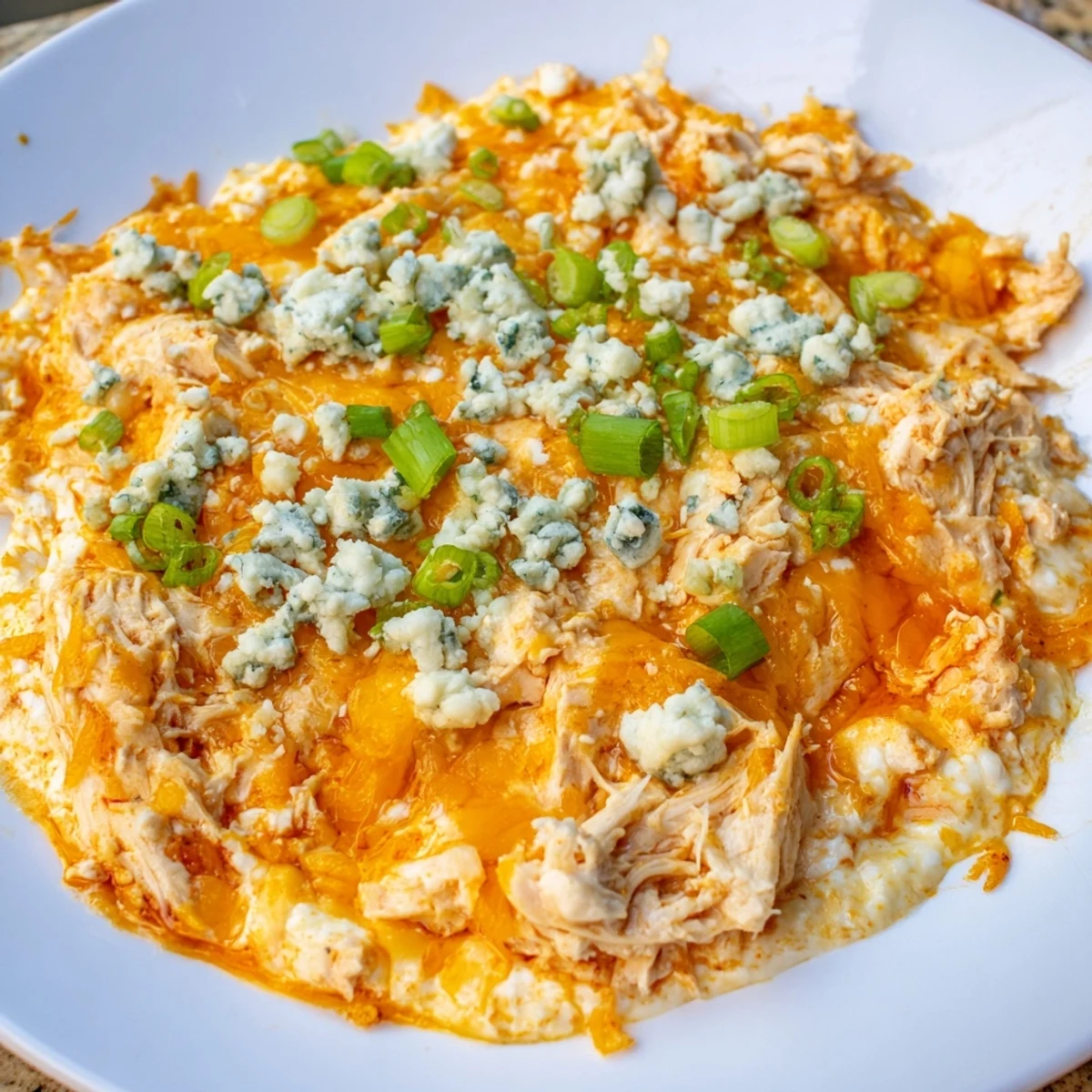A spoonful of creamy Keto Buffalo Chicken Dip is lifted from a golden-brown baked casserole, revealing tender shredded chicken inside.