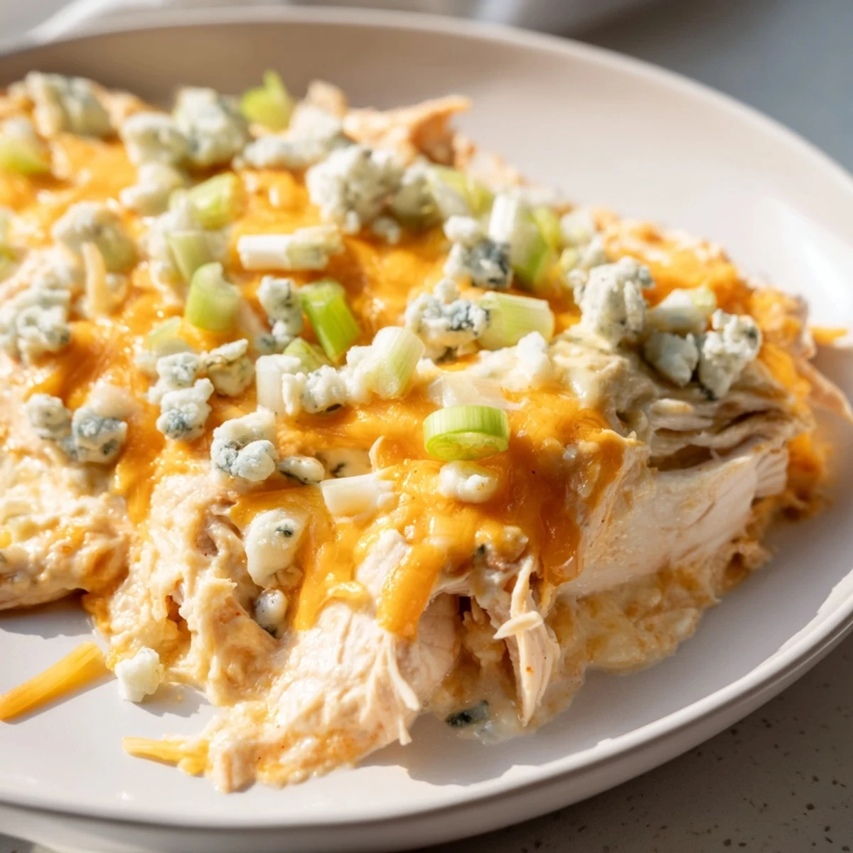 A freshly baked Keto Buffalo Chicken Dip, garnished with crumbled blue cheese and green onions, ready to be scooped with keto crackers.