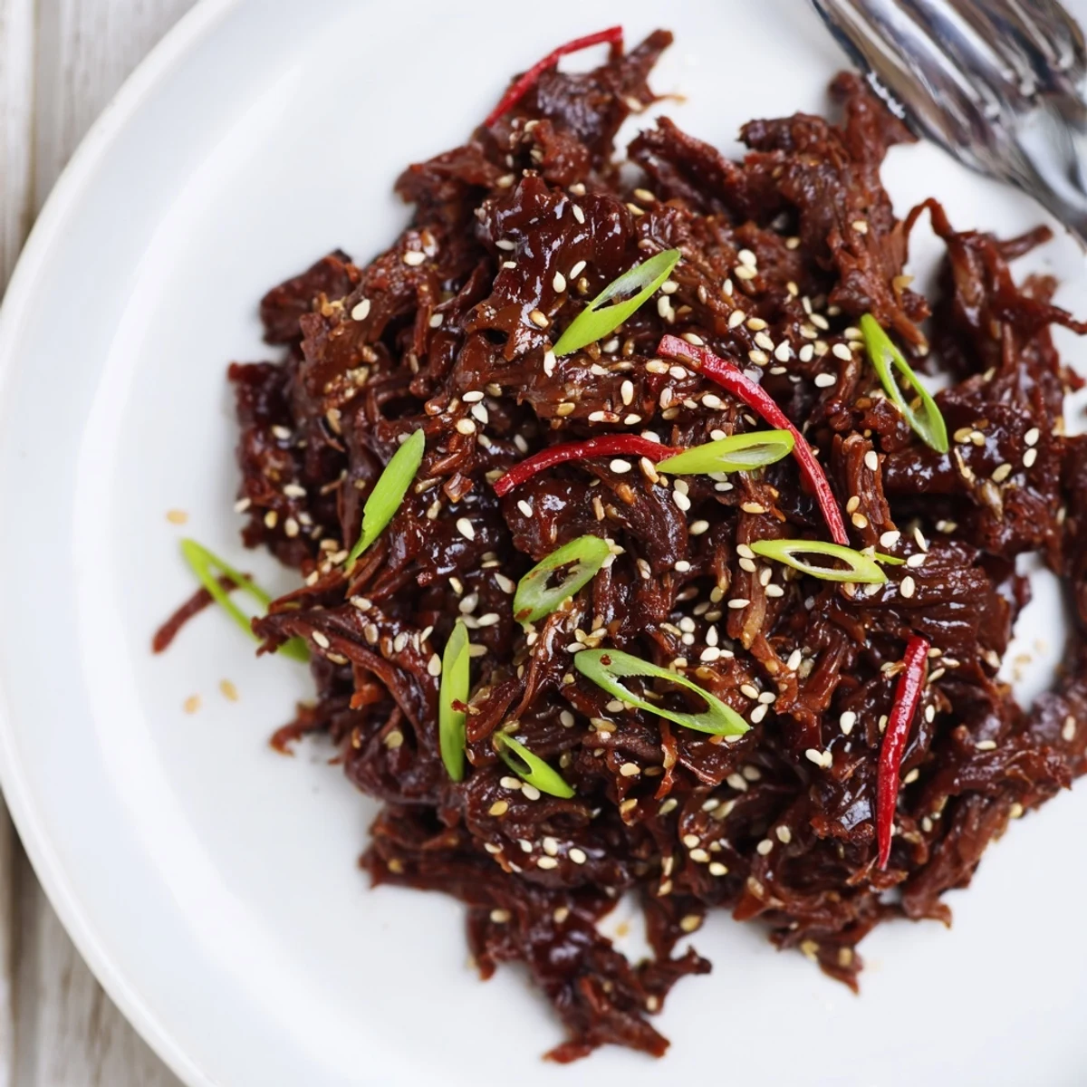 A fork lifts tender Slow Cooker Korean Beef from a slow cooker, showcasing savory sauce and garnishes in warm lighting.