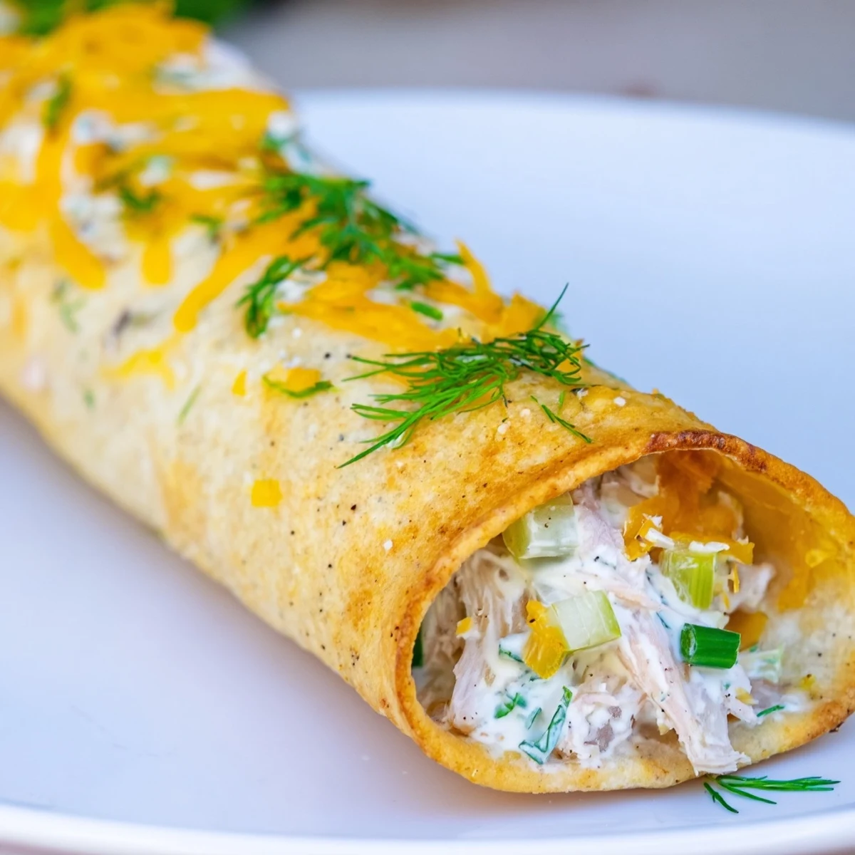 Close-up of a broken Dill Pickle Ranch Chicken Taquito revealing tender shredded chicken, chopped pickles, and green onion specks.