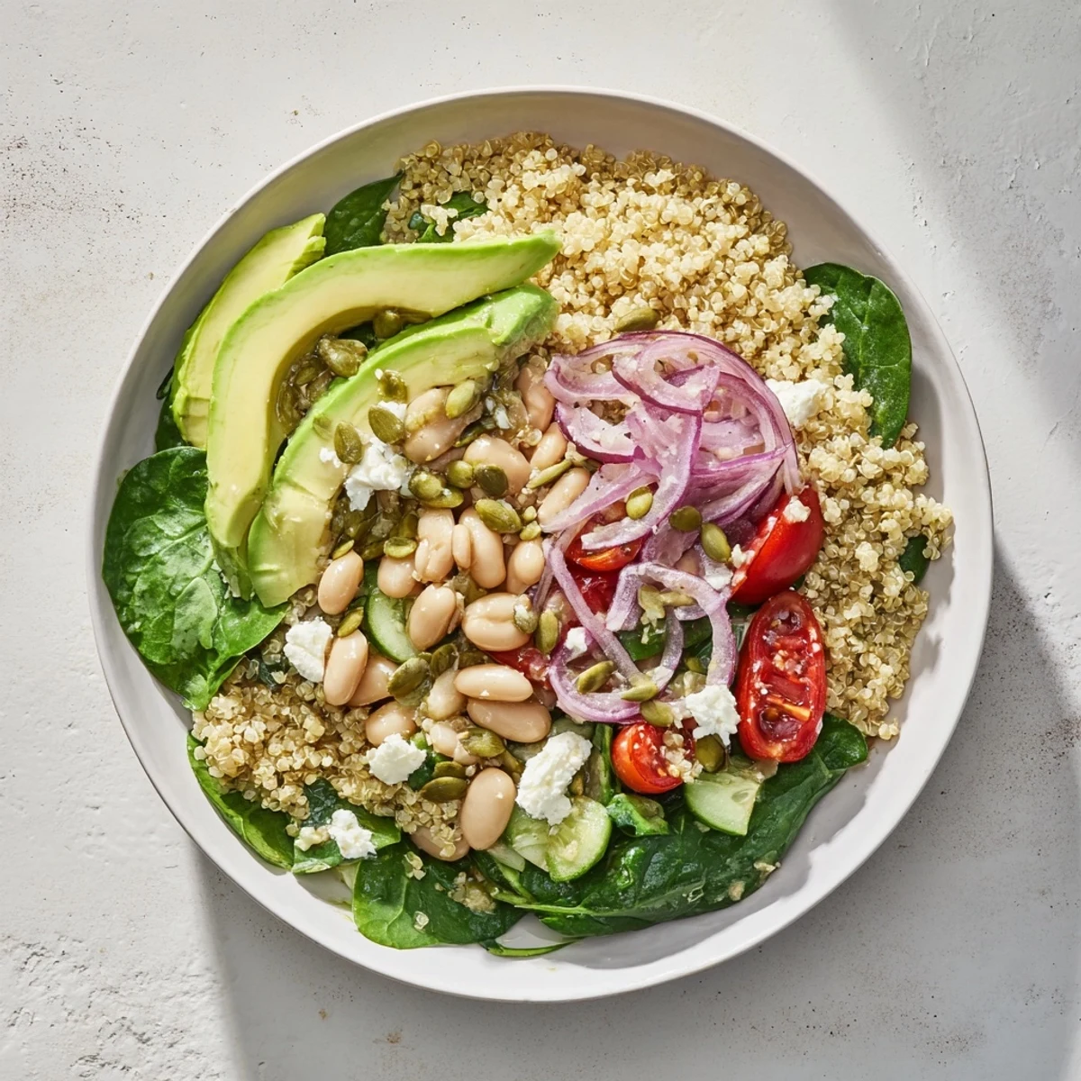 Freshly cooked quinoa topped with baby spinach, white beans, cherry tomatoes, and creamy avocado slices for a vibrant meal.