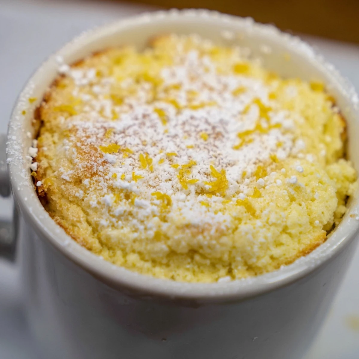 Single-serving Lemon Cottage Cheese Mug Cake with a dollop of yogurt and fresh lemon slices for a light dessert.