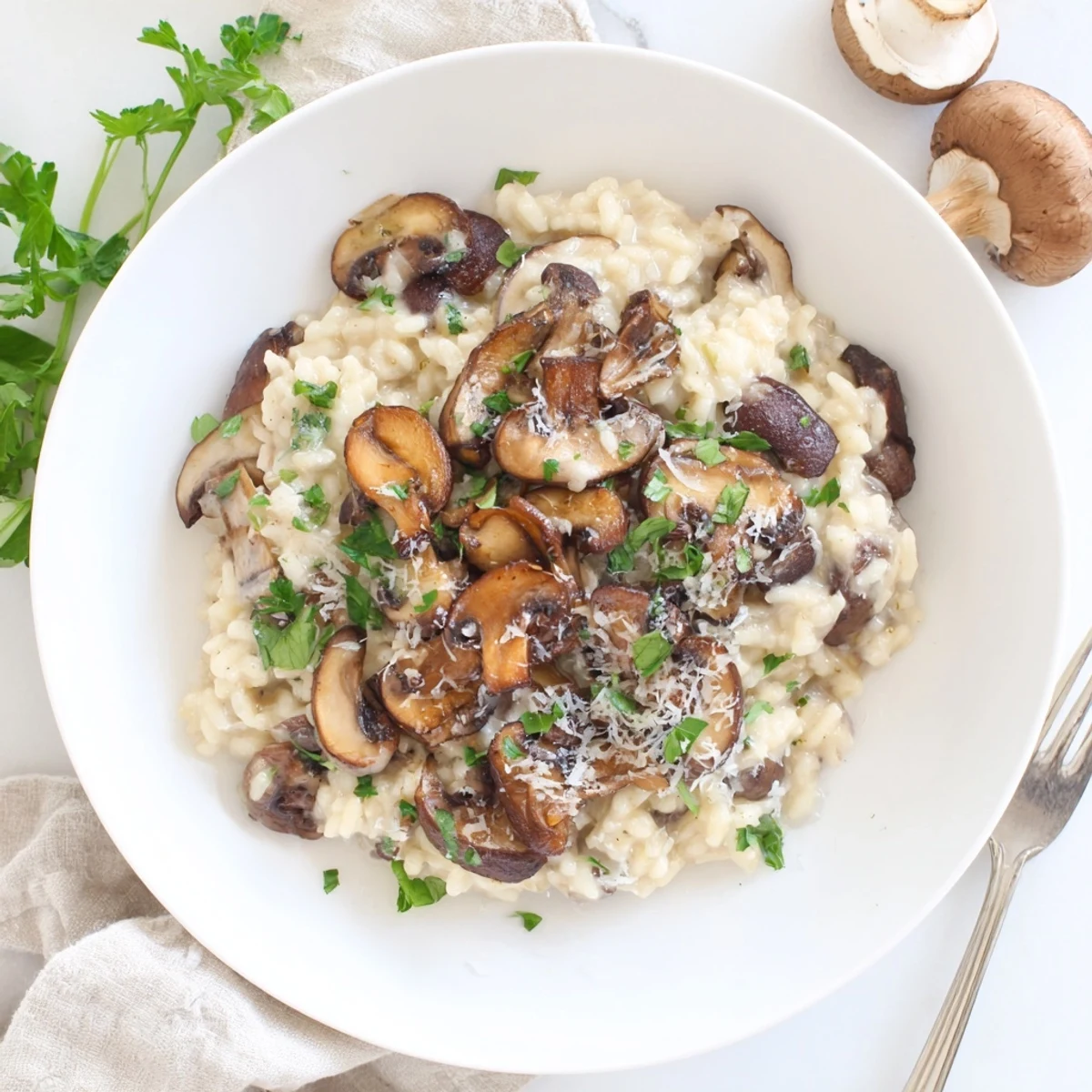 A close-up of creamy mushroom risotto in a white bowl, garnished with fresh parsley and extra Parmesan, ready to serve.
