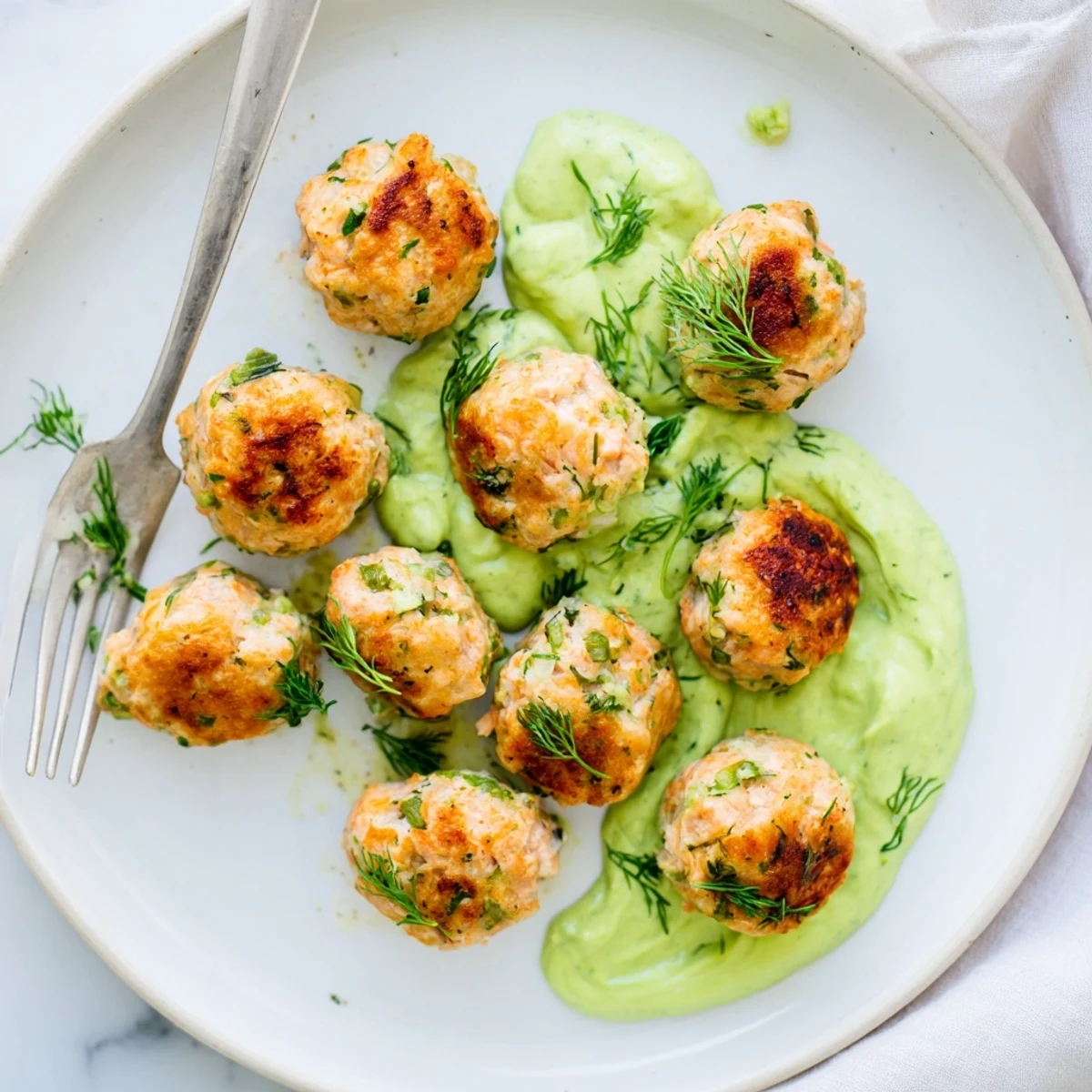 Freshly prepared Salmon Balls being dipped into a smooth avocado yogurt sauce, garnished with chopped cilantro for a light appetizer.