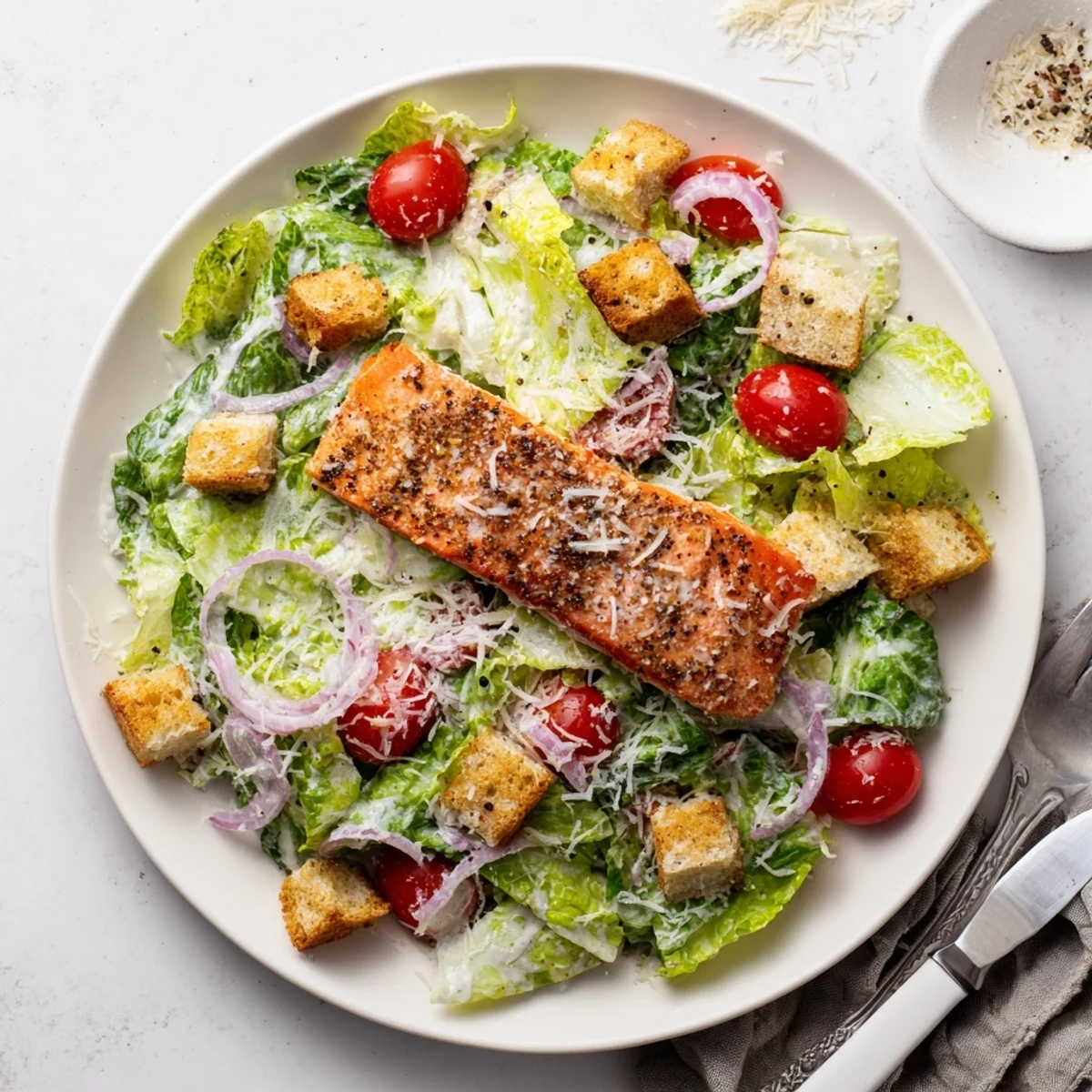 A close-up of Salmon Caesar Salad with grilled salmon fillet, crisp romaine, croutons, and creamy homemade dressing on a white plate.  