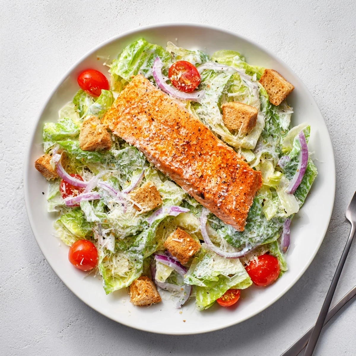 Overhead view of vibrant Salmon Caesar Salad with juicy grilled salmon, crunchy croutons, and drizzled Caesar dressing on a rustic table.