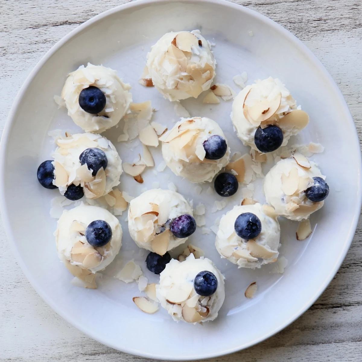 Blueberry Greek Yogurt Bites arranged on a chilled plate with sliced almonds and fresh berries.  