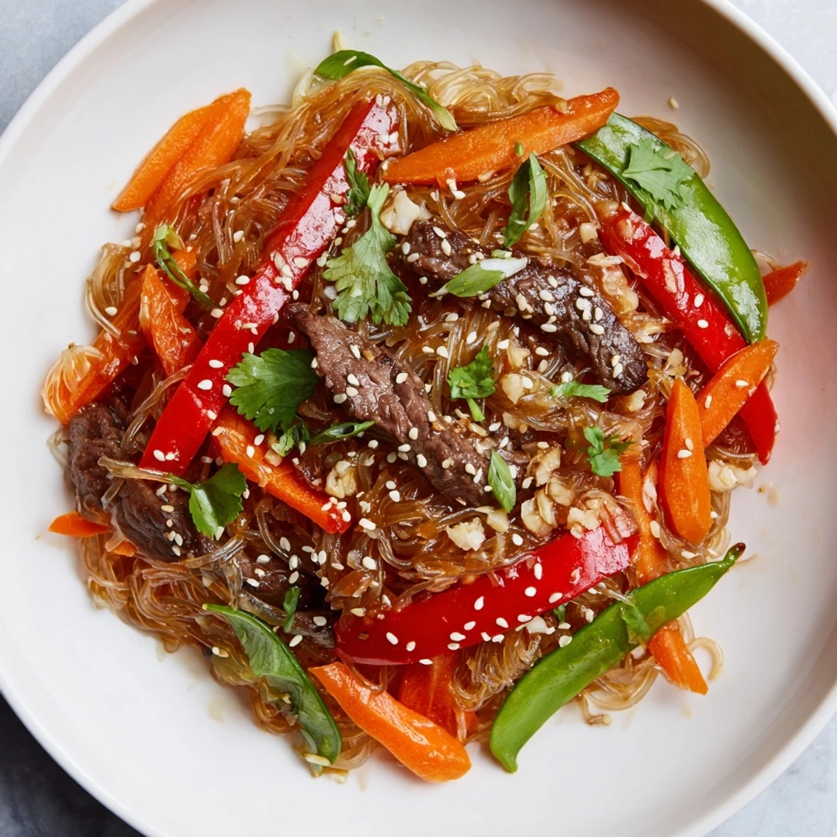 Steaming bowl of Asian-style sticky beef noodles garnished with sesame seeds and fresh cilantro on white background