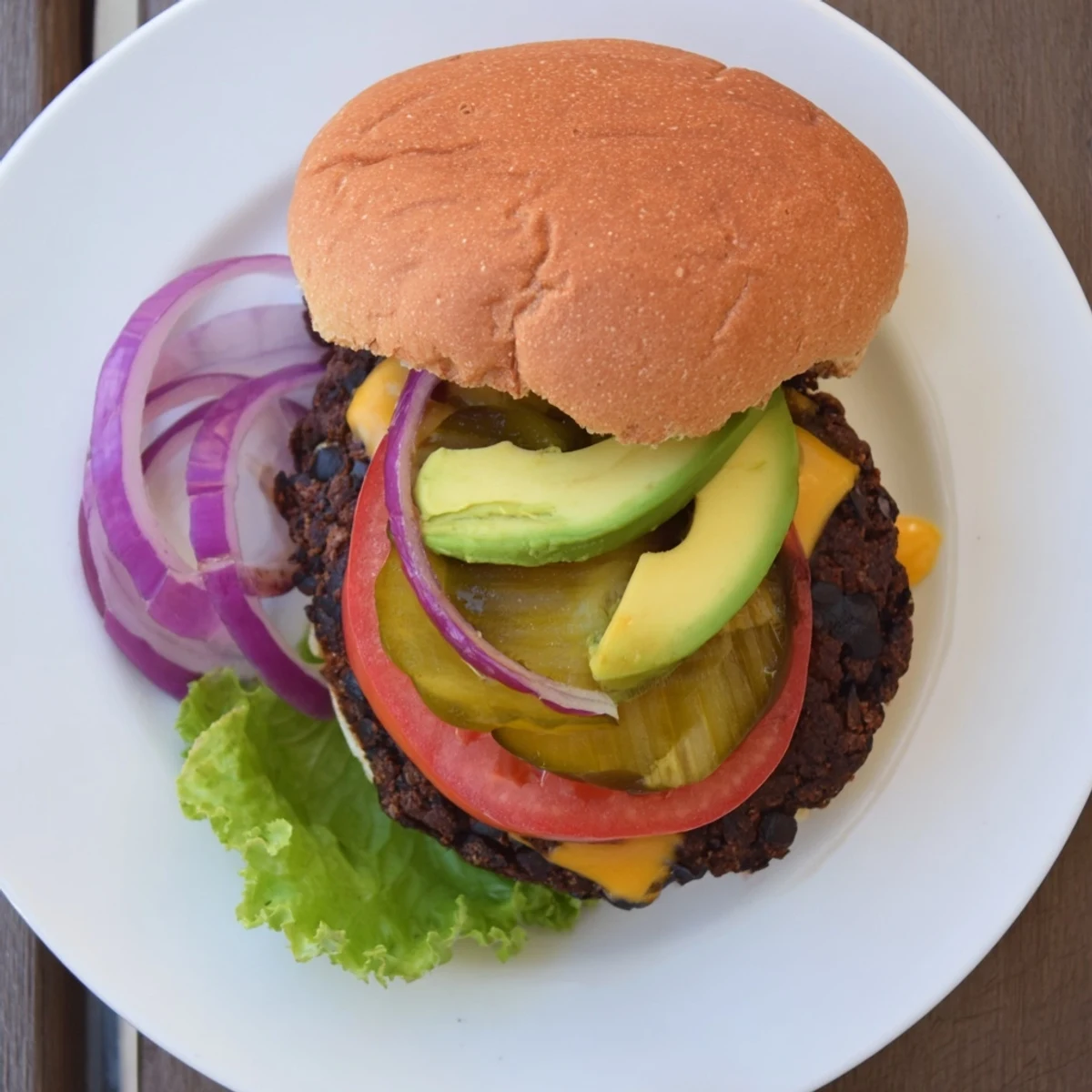 Vegetarian black bean burger with melted cheese, ripe avocado, and crunchy red onion served on a toasted brioche bun.
