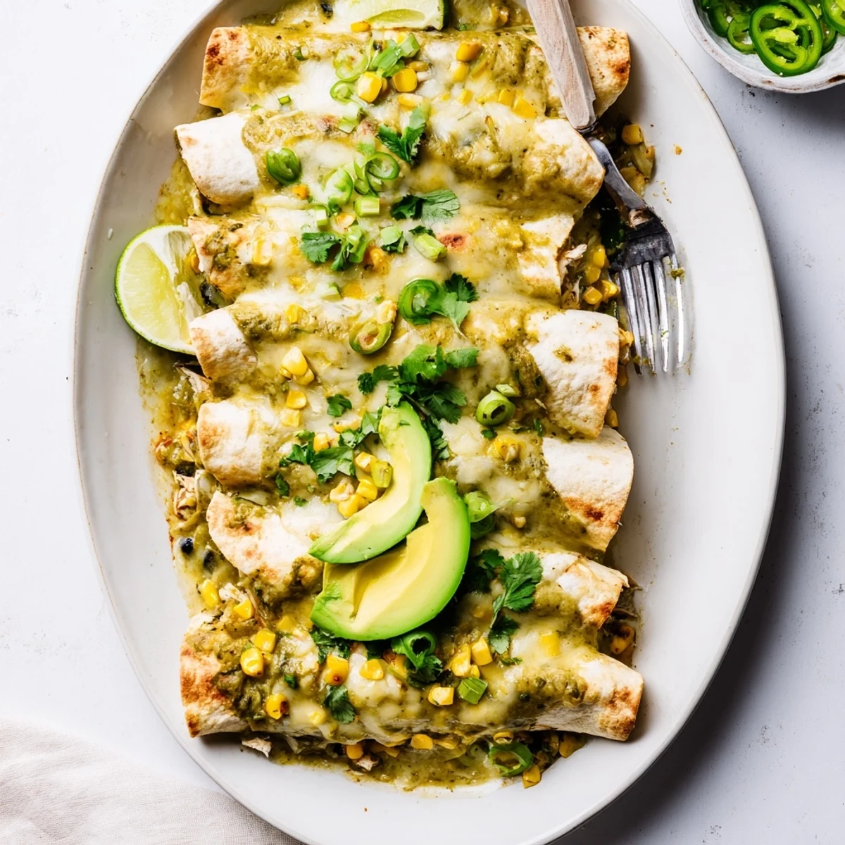 Oven-baked chicken enchiladas smothered in tangy green salsa and bubbling cheese sauce in baking dish
