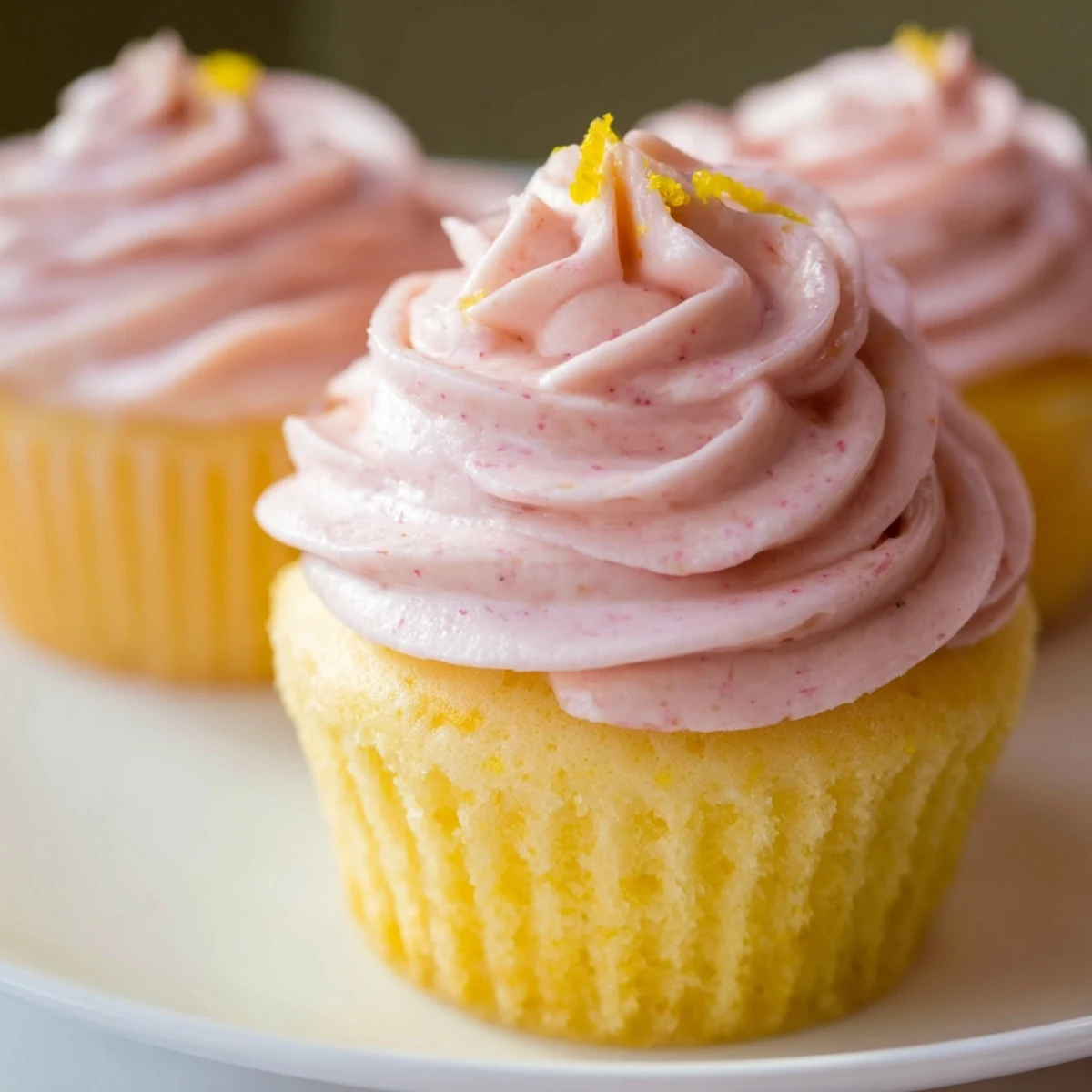 Golden lemon cupcakes swirled with pink strawberry buttercream on a white pedestal plate
