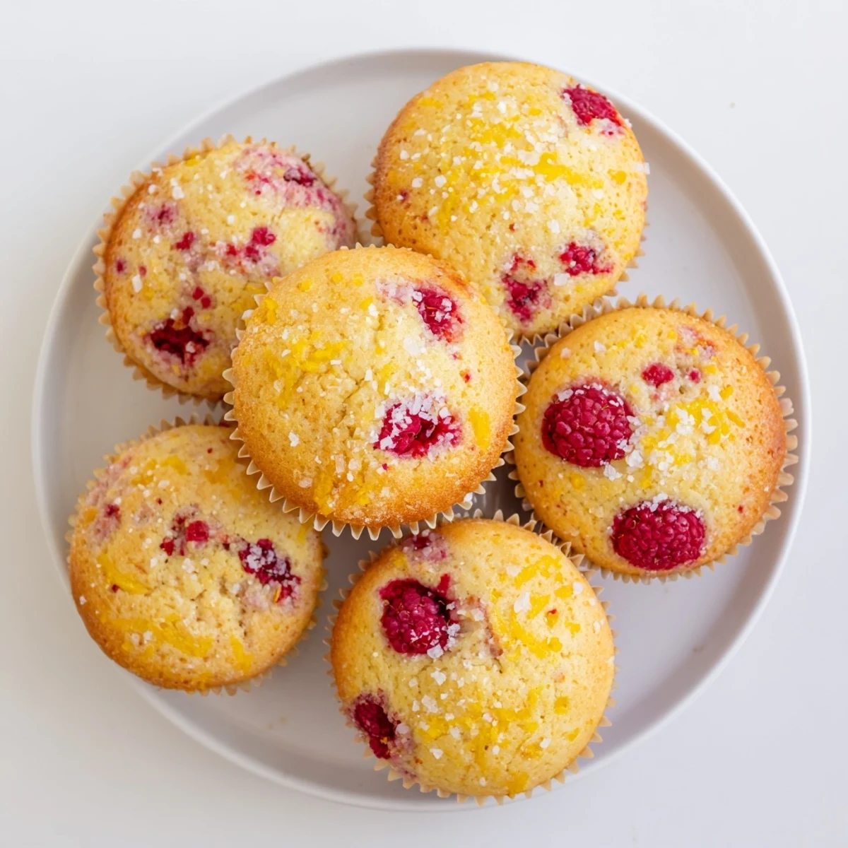 Freshly baked lemon raspberry muffins cooling on a wire rack with vibrant red berry pieces