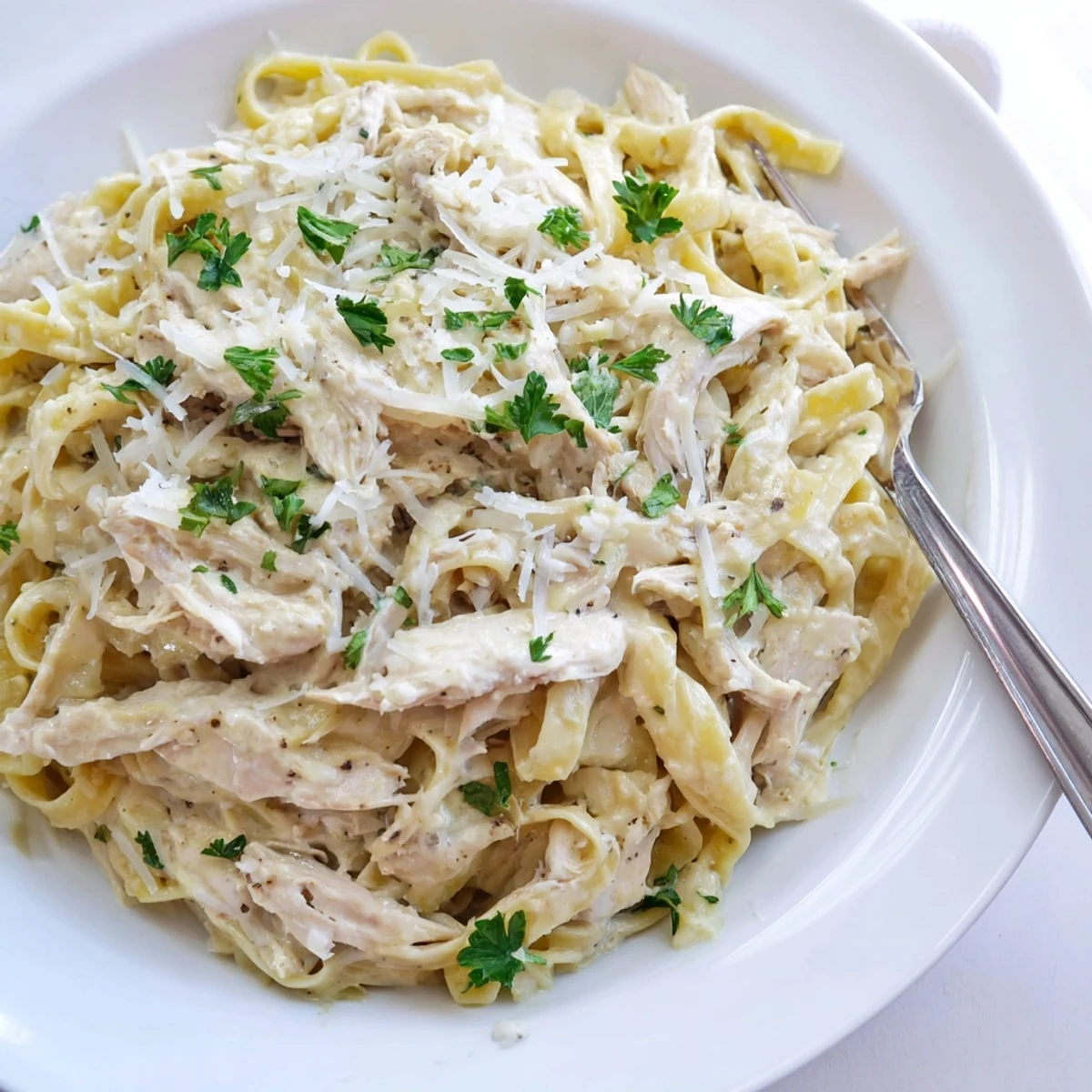 Creamy Crock Pot Chicken Alfredo with tender shredded fettuccine noodles and melted parmesan cheese garnished with fresh parsley
