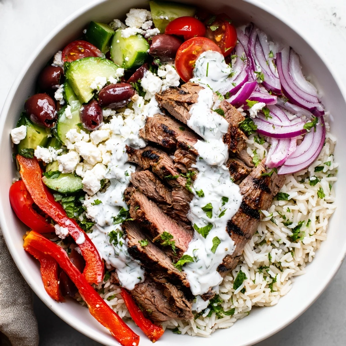 Colorful Mediterranean steak bowl featuring grilled sliced steak over herbed rice with fresh tomatoes, cucumber, olives, and creamy feta cheese.