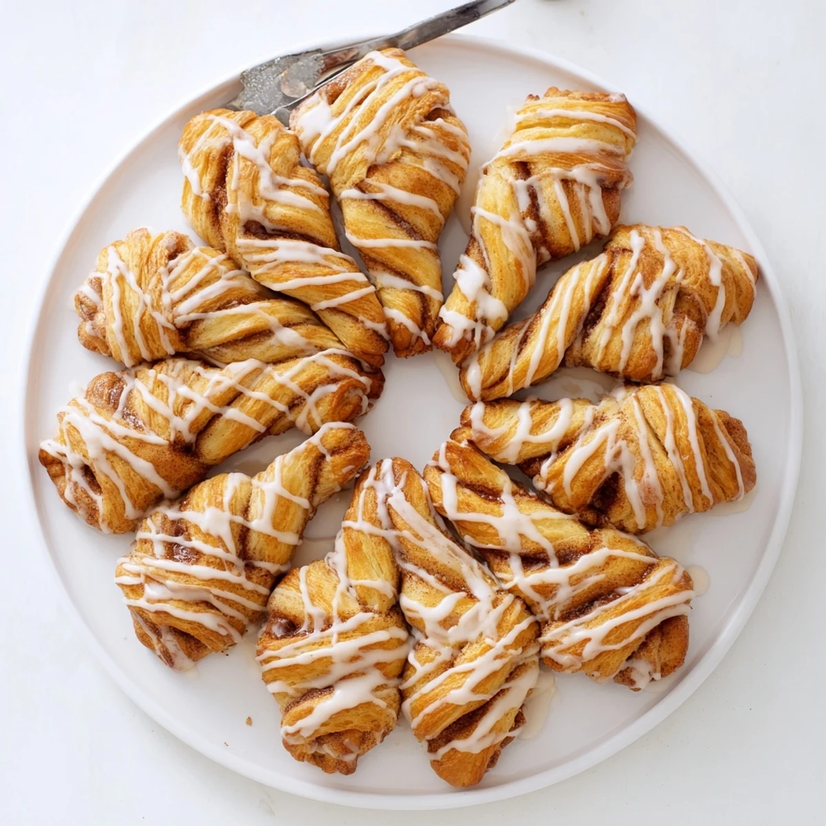 Golden sweet cinnamon twists drizzled with vanilla glaze on a white serving plate
