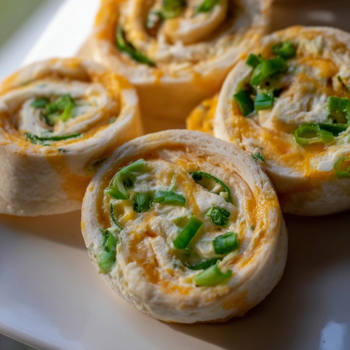 Golden baked jalapeno popper pinwheels arranged on a white serving platter with fresh cilantro garnish