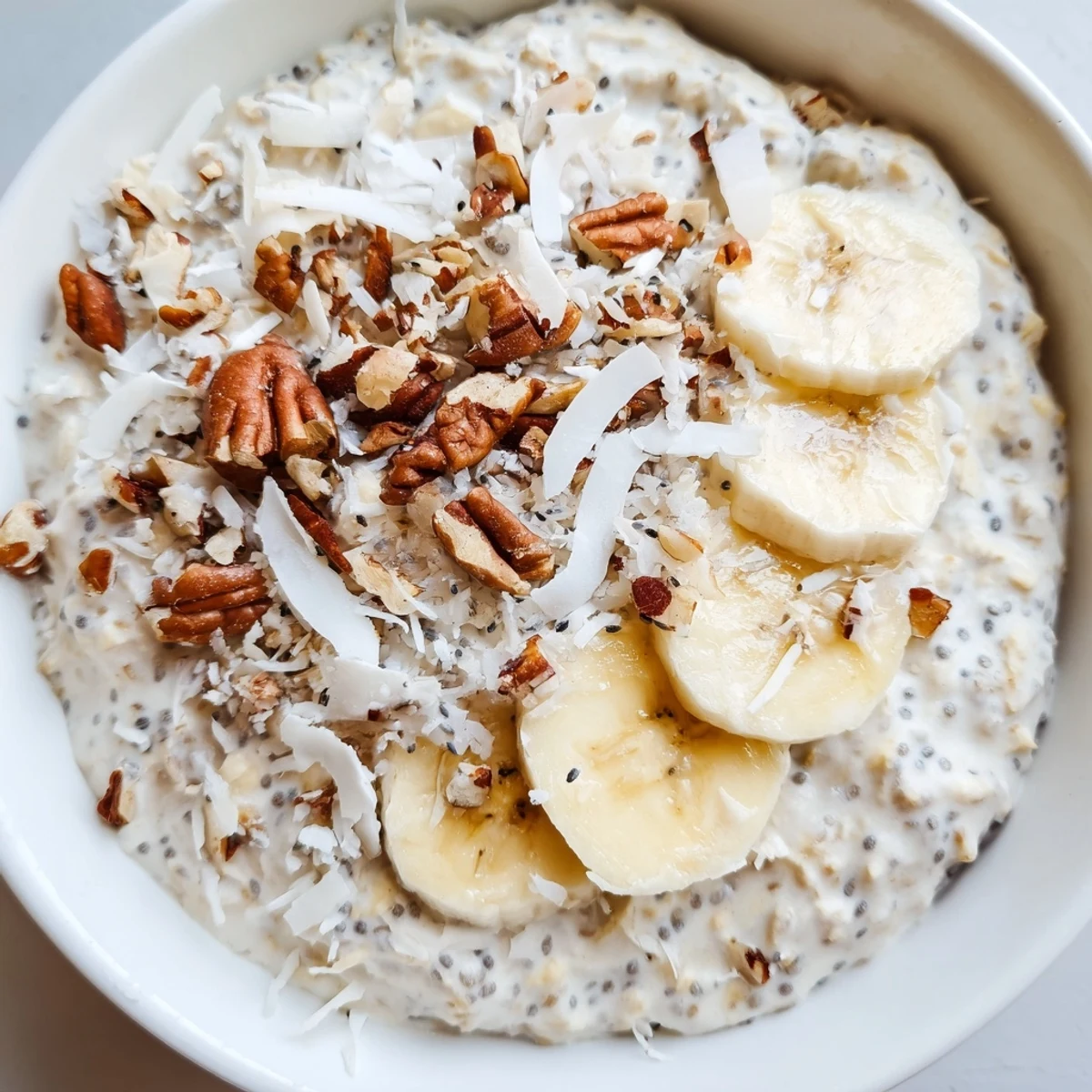 Creamy coconut cream pie overnight oats topped with toasted coconut flakes and crunchy pecans