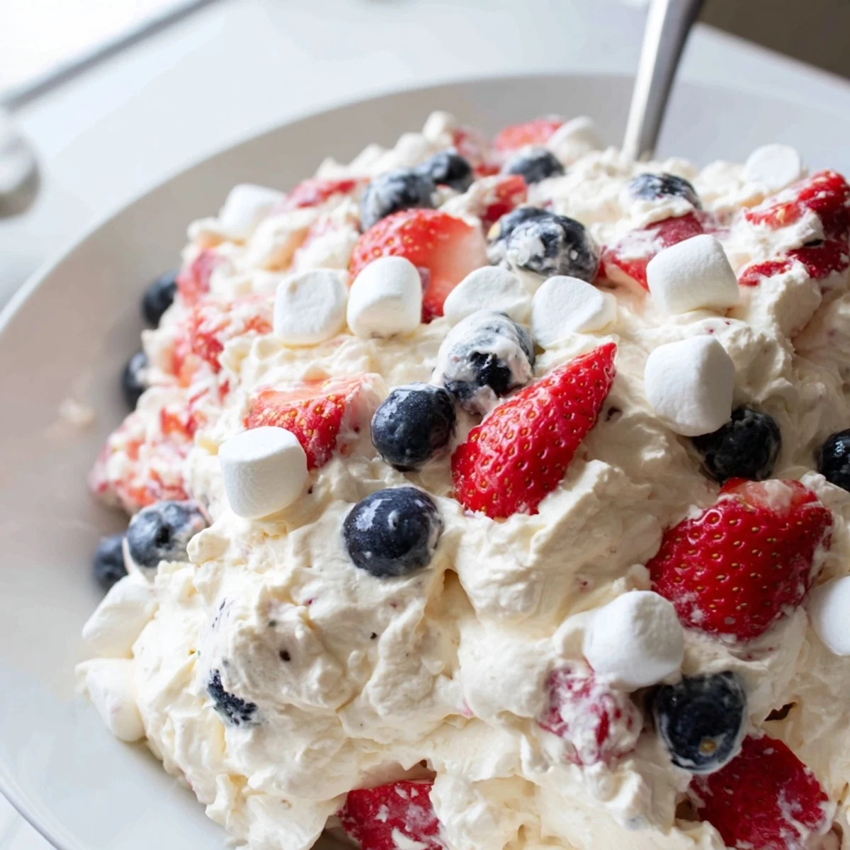 Red white blue cheesecake salad loaded with juicy strawberries blueberries and fluffy marshmallows in creamy dressing