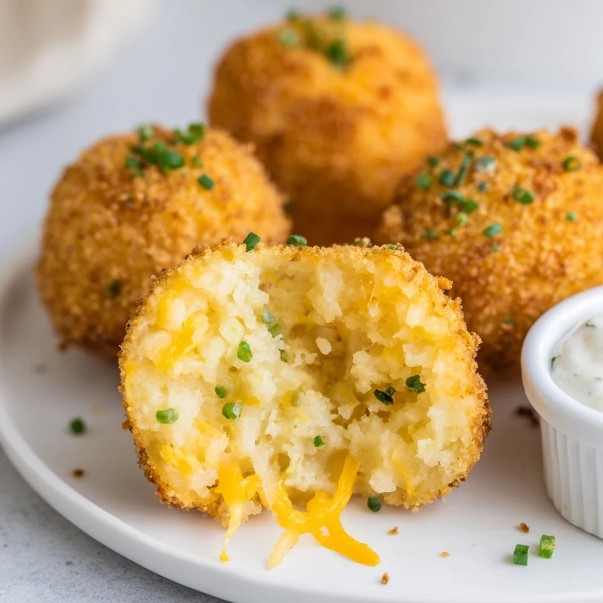 Handheld fried mashed potato balls plated with spicy ketchup and green onions