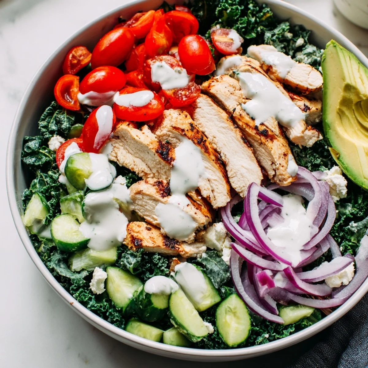 Nourishing marinated kale and chicken bowl topped with avocado, tomatoes, and creamy dressing