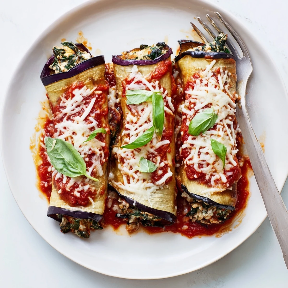 Baked Healthy Eggplant Rollatini plated warm, golden cheese, fresh basil garnish.