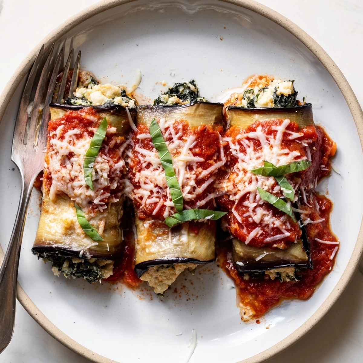 Hearty Healthy Eggplant Rollatini resting after baking, tangy marinara and melted mozzarella.