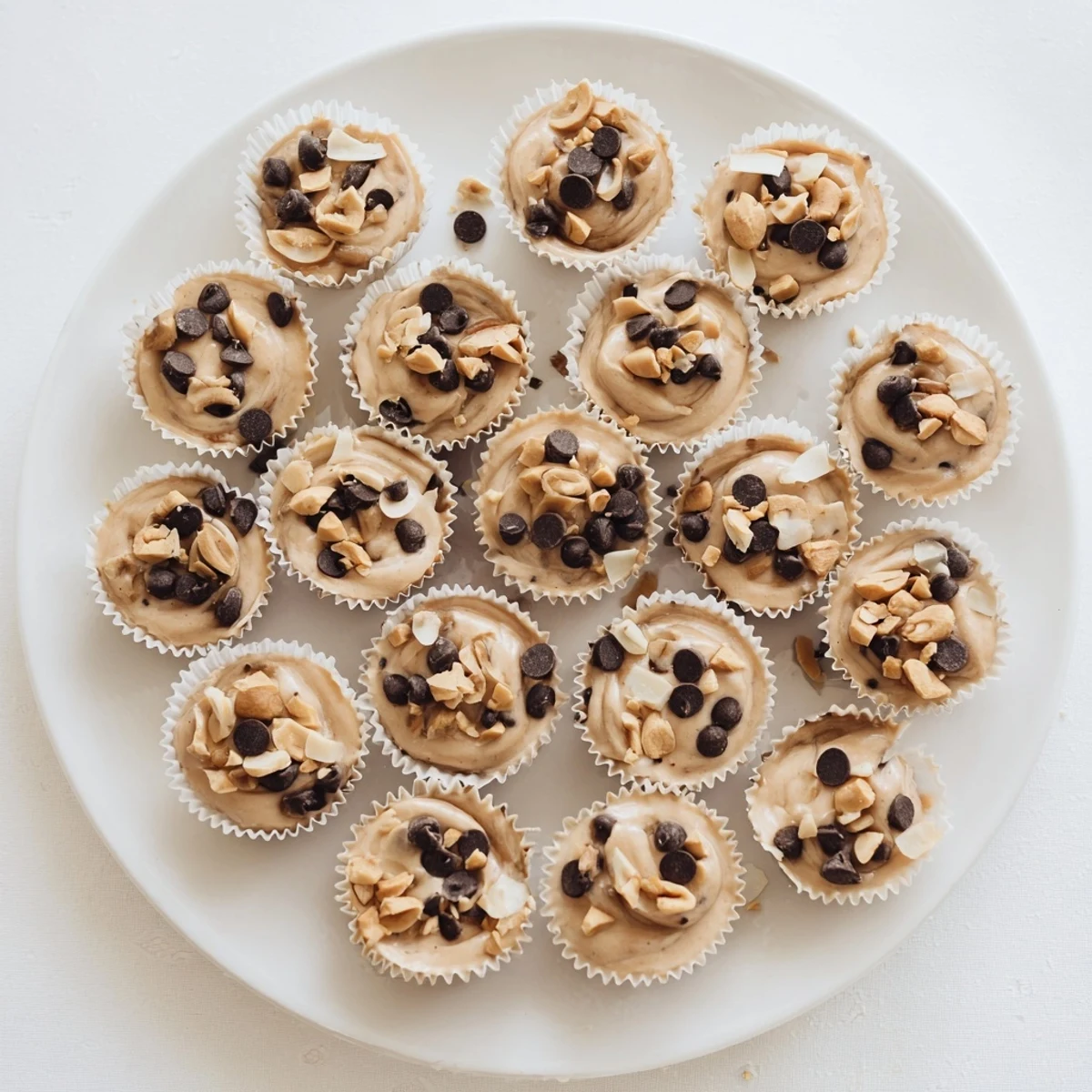 Frozen peanut butter Greek yogurt bites arranged on a white plate topped with melted chocolate chips and crushed roasted peanuts
