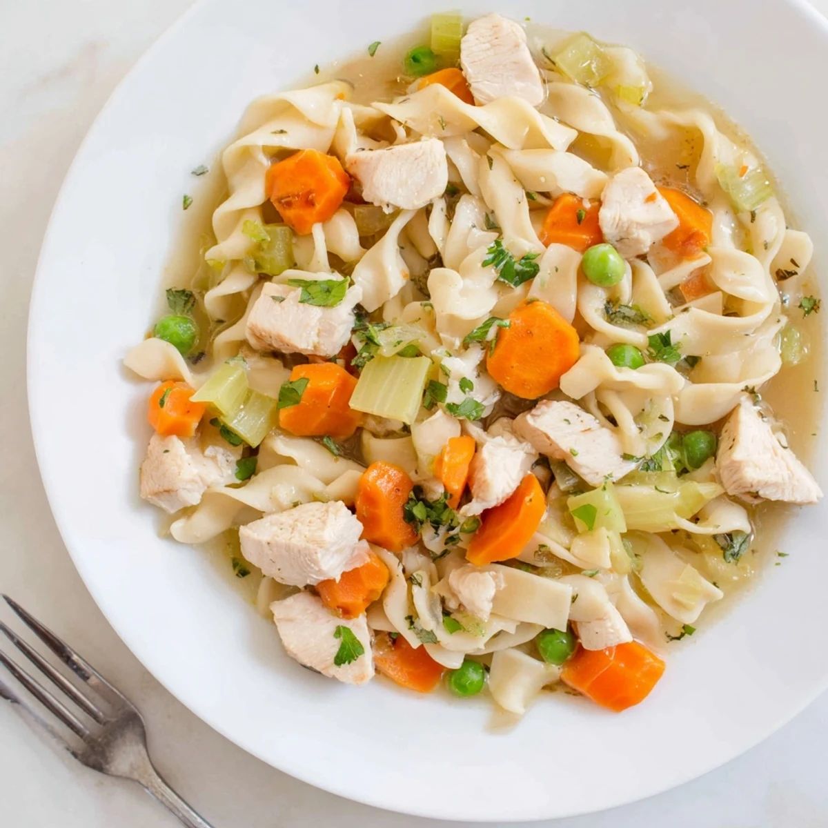 Hearty one pot chicken and noodles served hot with peas and fresh parsley garnish