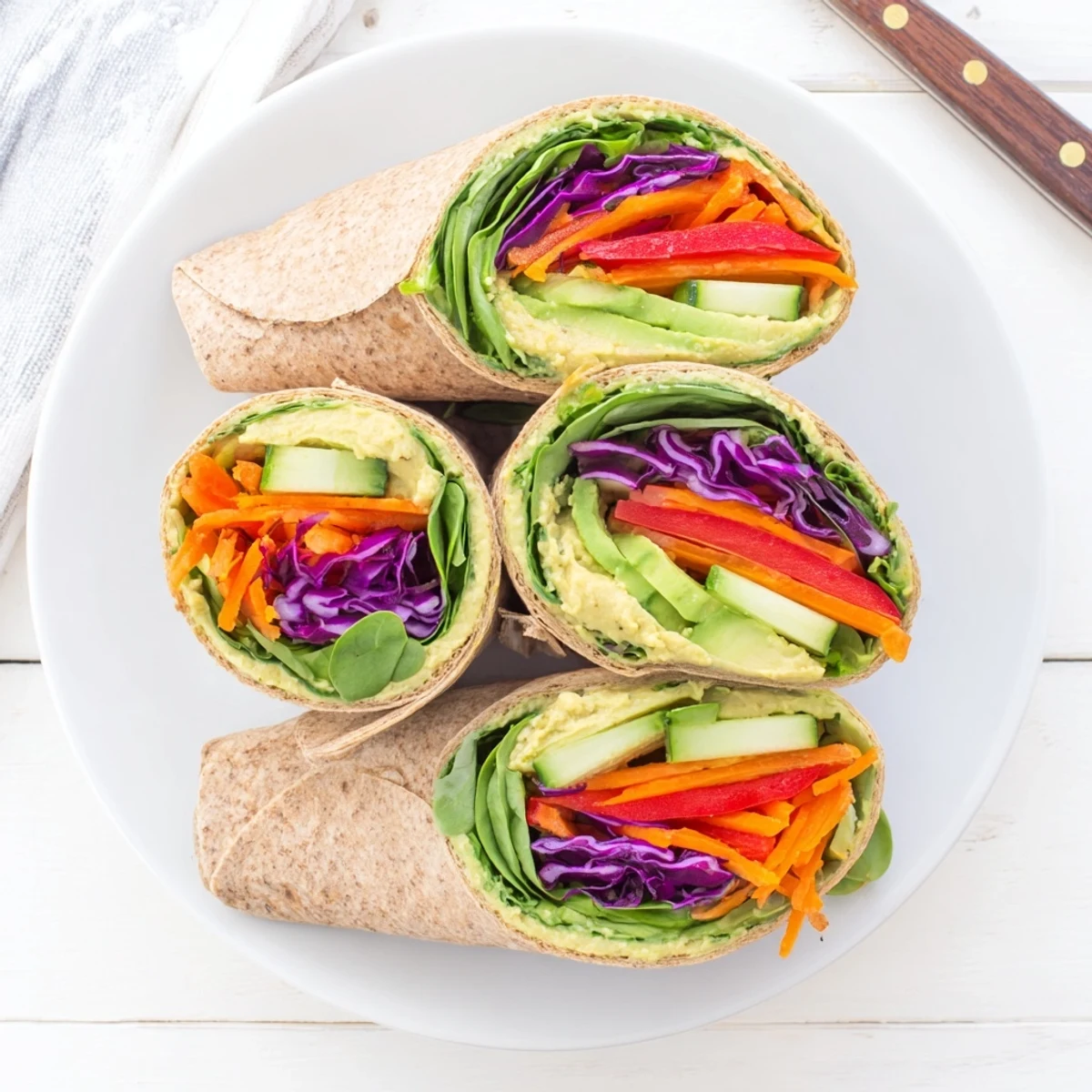 Sliced veggie wrap with hummus revealing vibrant rainbow vegetables wrapped in soft flour tortilla