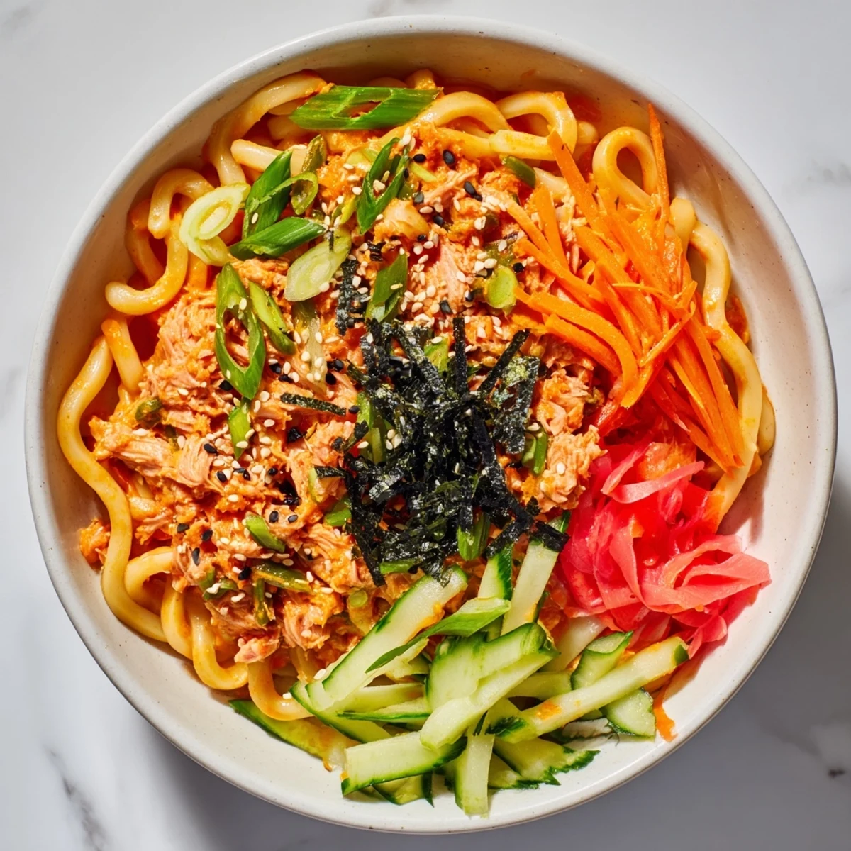 Chilled spicy tuna udon bowl featuring thick wheat noodles coated in creamy mayonnaise-based sauce with crunchy spring onions