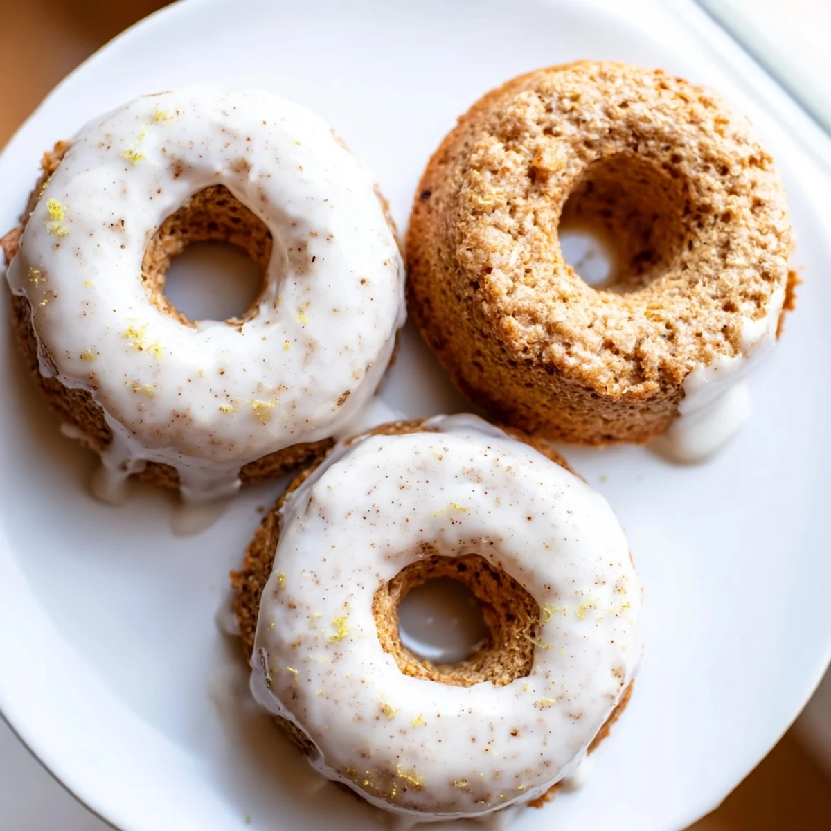 Golden banana bread donuts topped with sweet vanilla glaze and sprinkled with cinnamon on a white plate