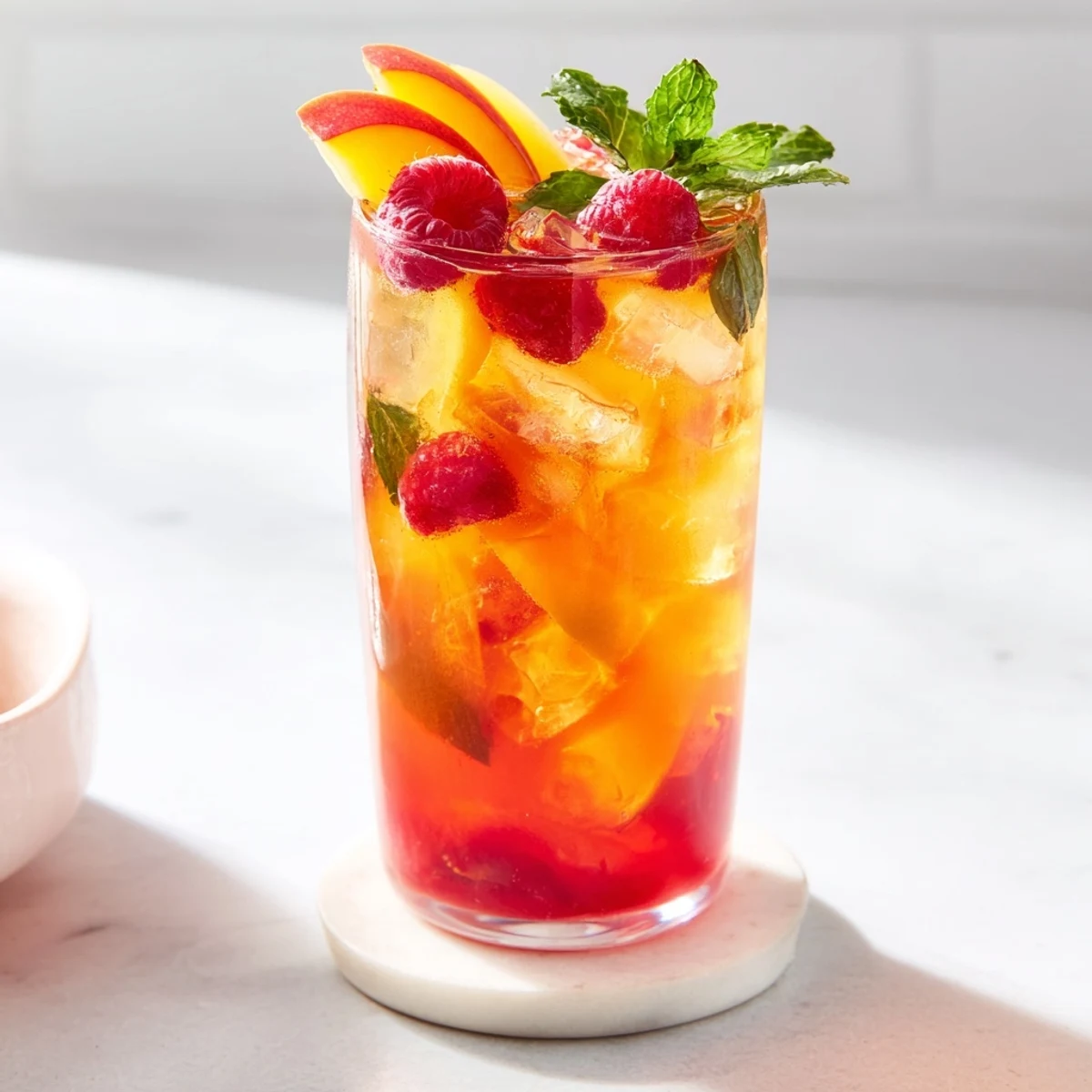 Garnished glass of raspberry peach iced tea lemonade with fresh fruit slices and mint