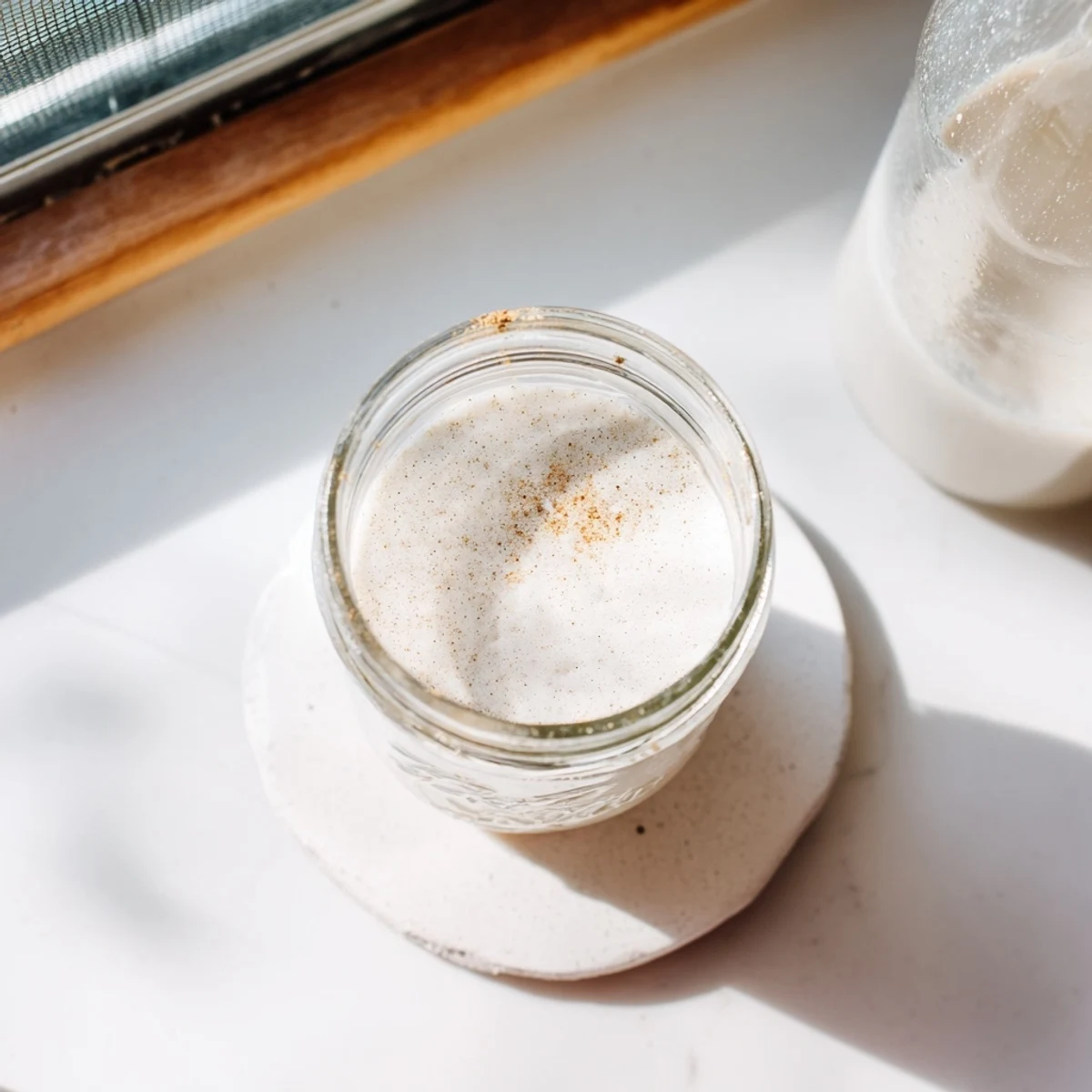 Glass of fresh homemade almond milk with whole raw almonds scattered on a wooden kitchen counter