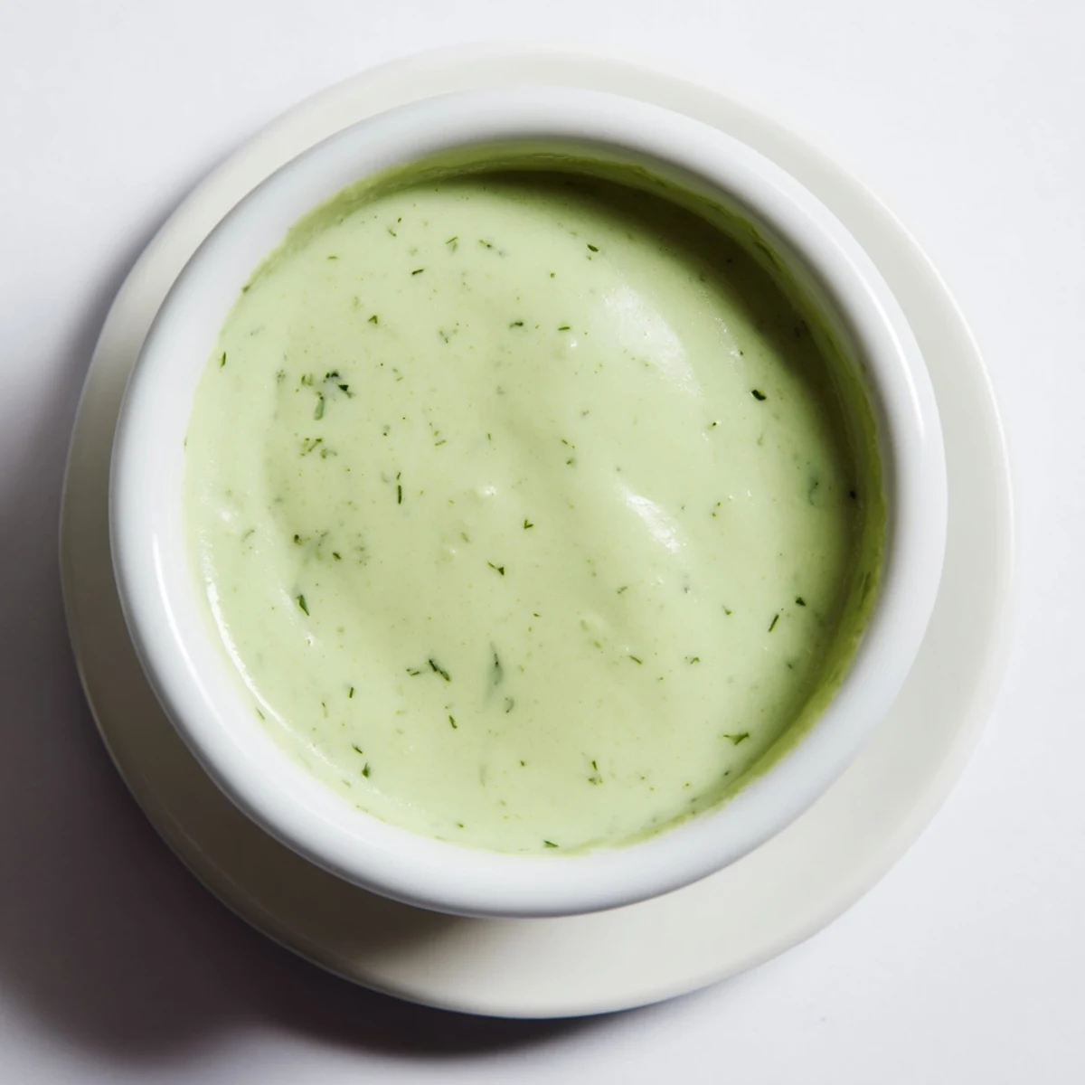 Creamy cilantro lime sauce in a white ramekin with a silver spoon, showing the vibrant green color and velvety texture beside fresh lime wedges