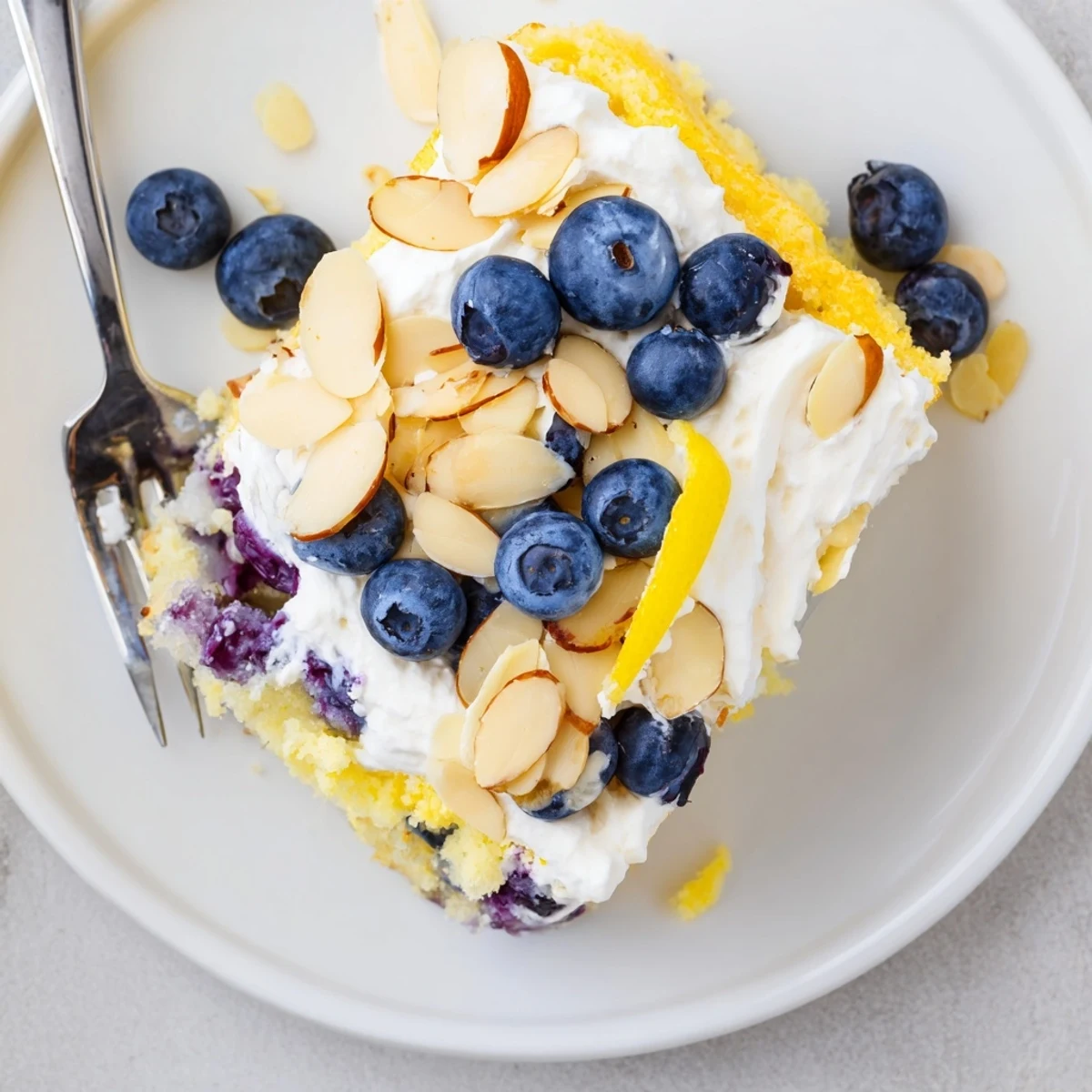 Golden lemon blueberry poke cake with fluffy whipped cream and toasted almond crunch