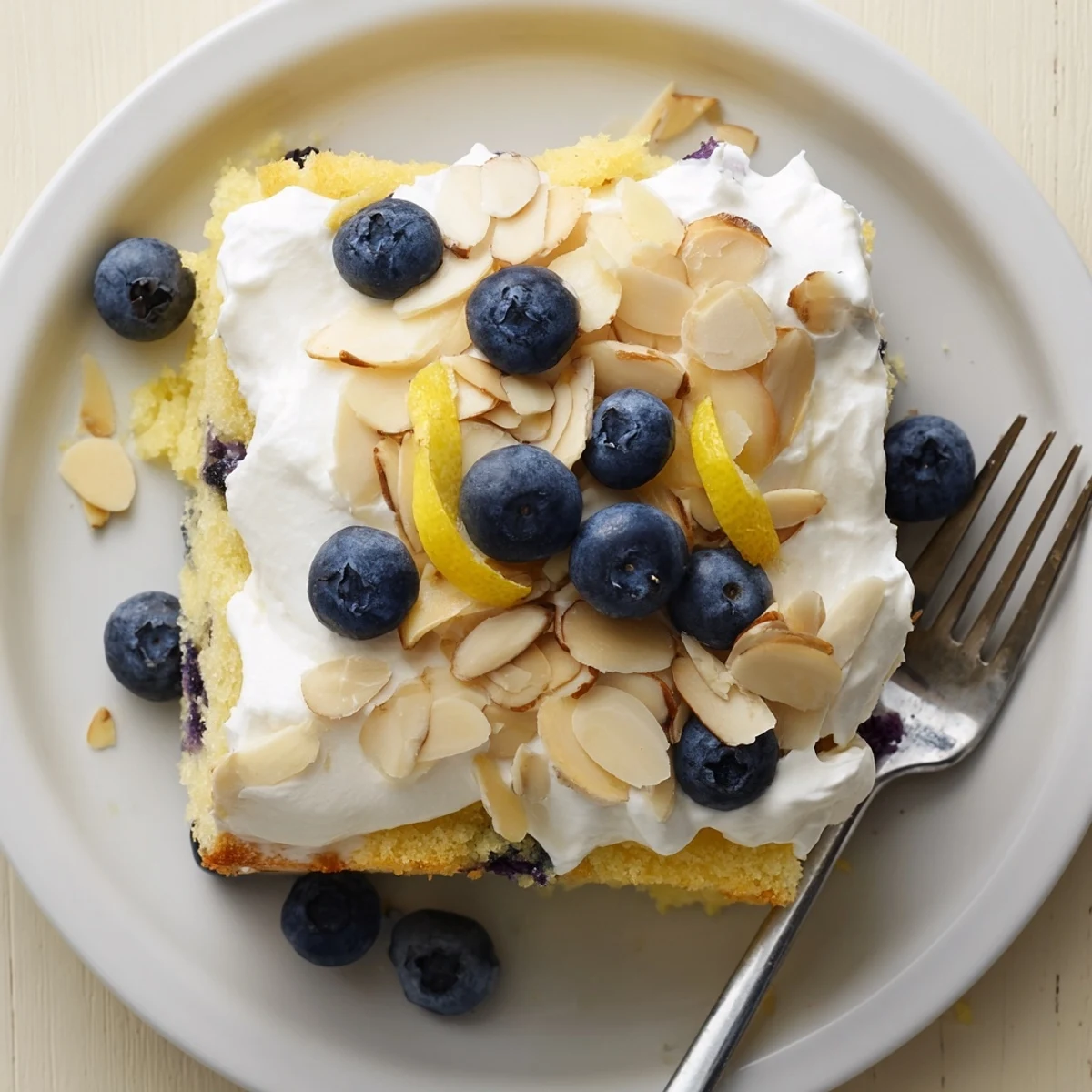 Slice of lemon blueberry poke cake showcasing whipped topping, blueberry bursts, and almonds