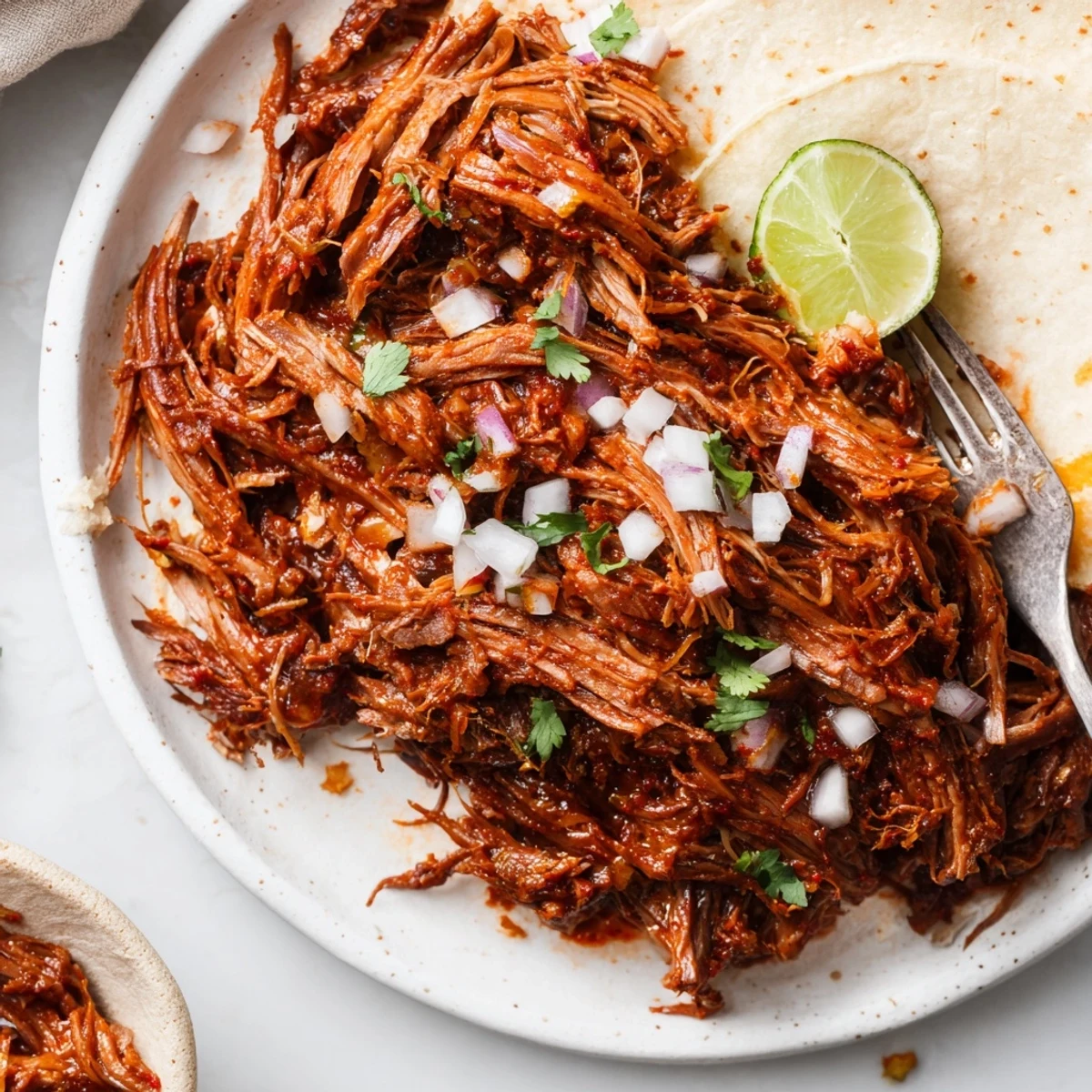 Shredded Slow Cooker Beef Barbacoa with chopped cilantro, onions, and lime wedges